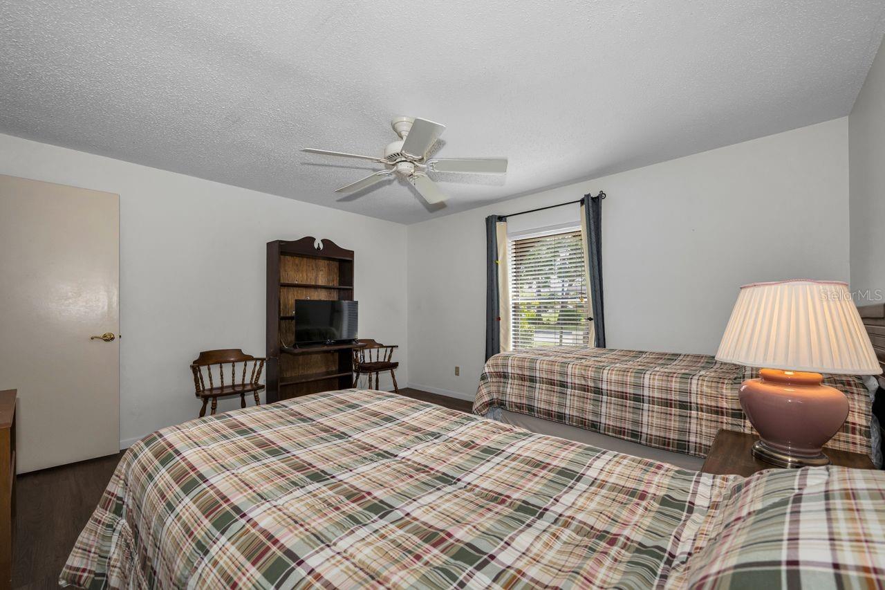 Bedroom with two plaid-covered beds, a television on a dark wood shelf, and a window with blinds.