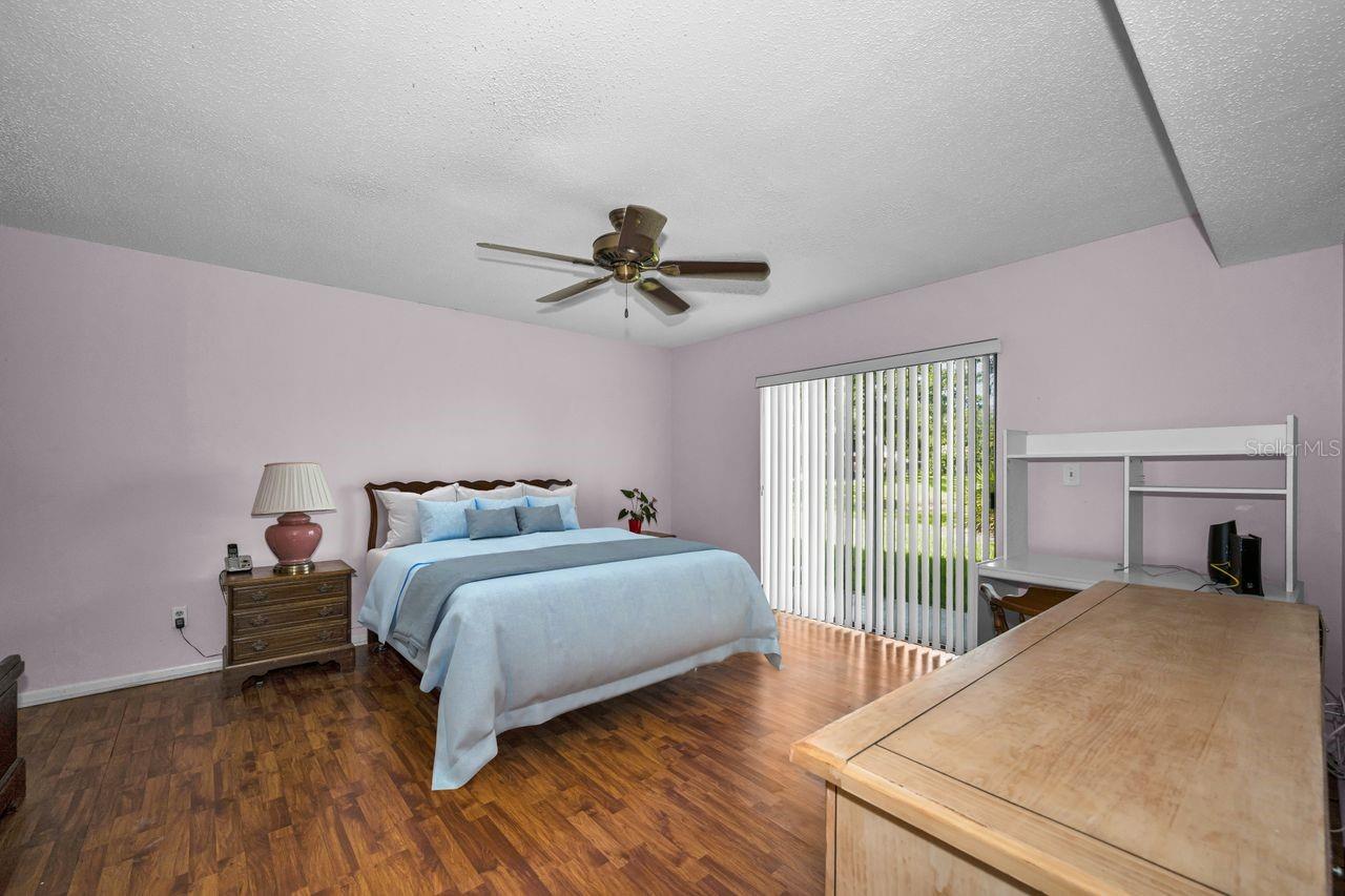 Bedroom with blue-and-white bedding, a ceiling fan, vertical blinds, and a large wooden desk.