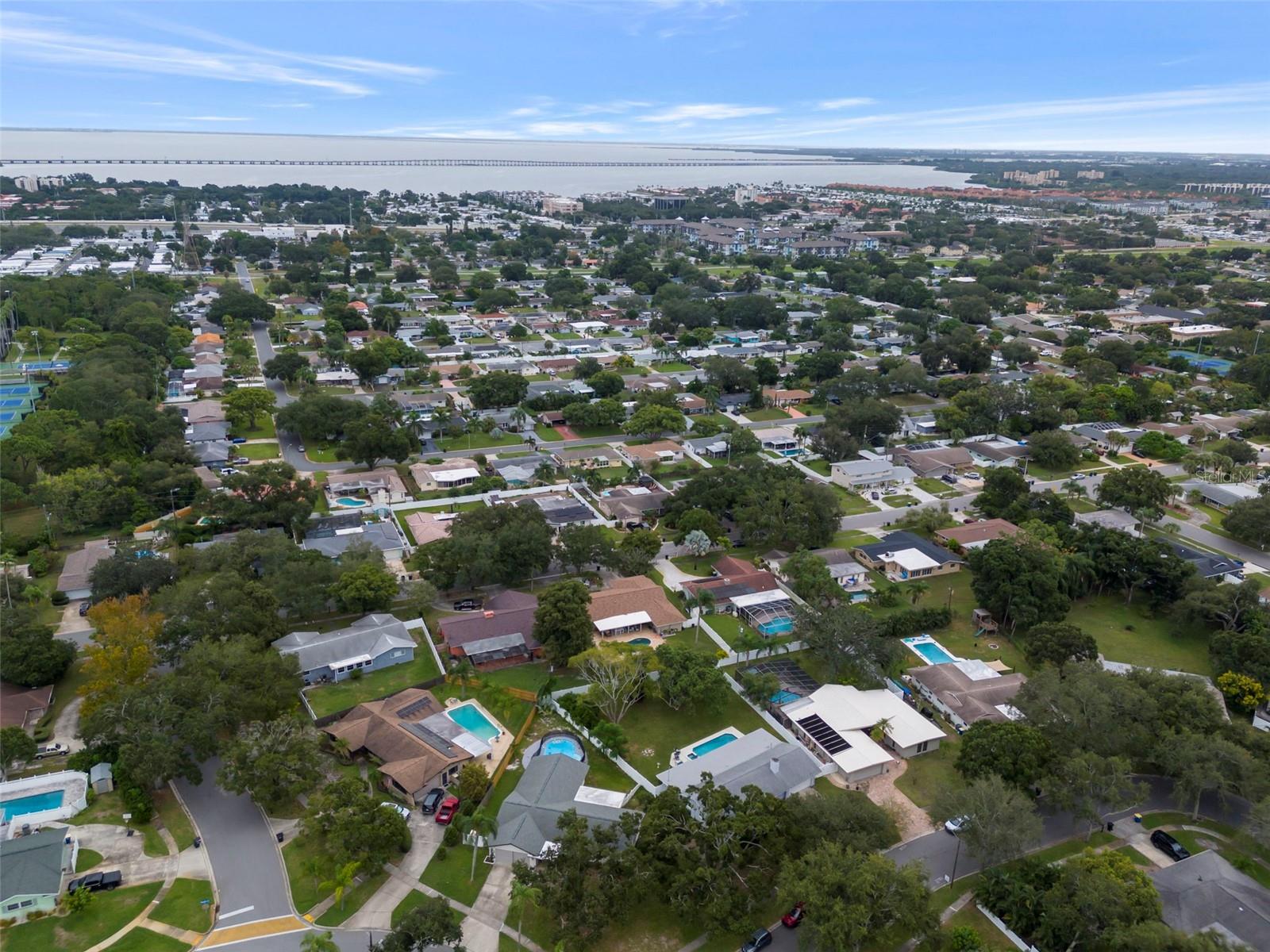 Aerial view of a residential neighborhood with backyard pools, a distant body of water, and a long bridge.