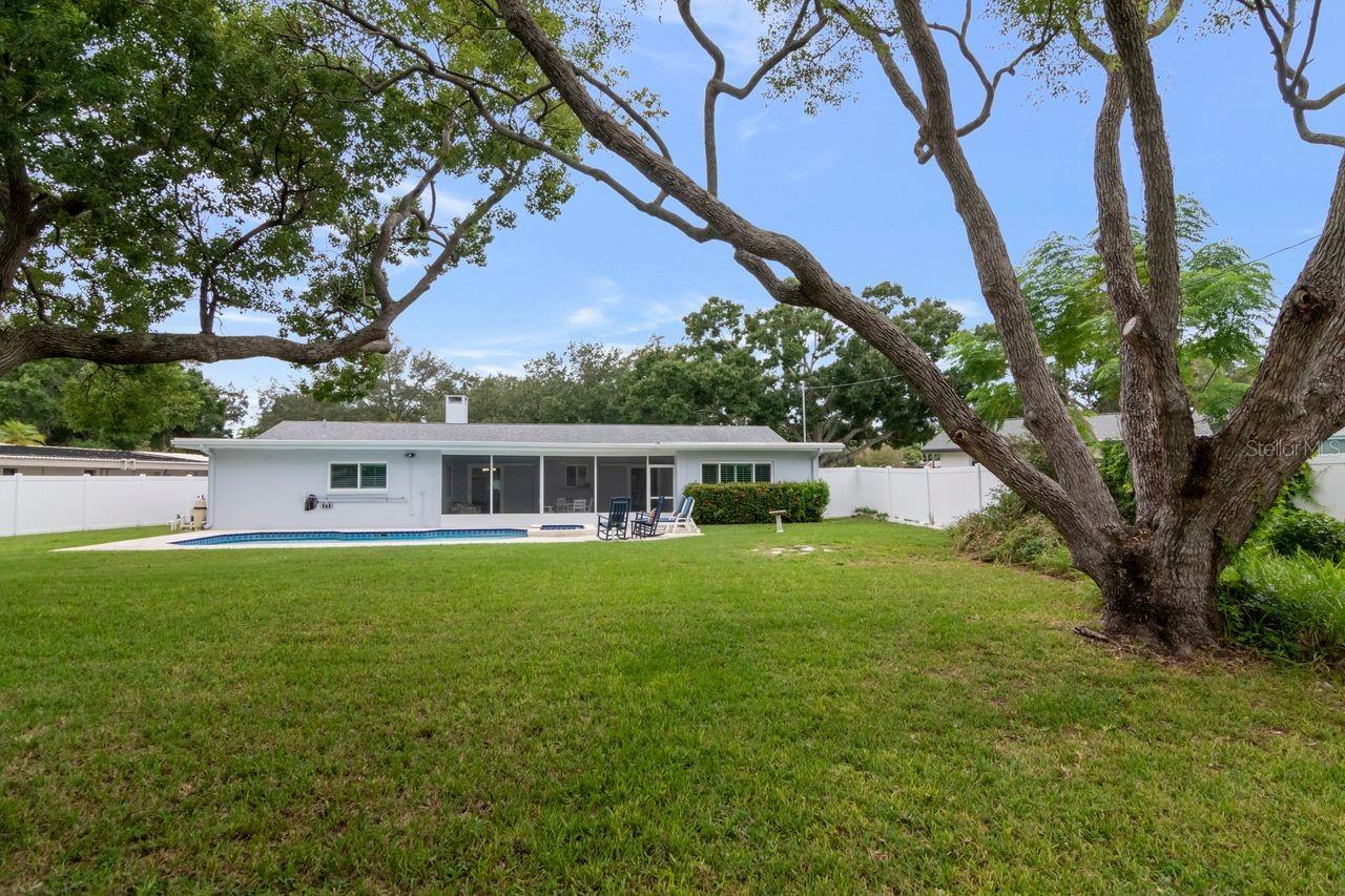 Backyard with a swimming pool behind a single-story home, framed by mature trees.