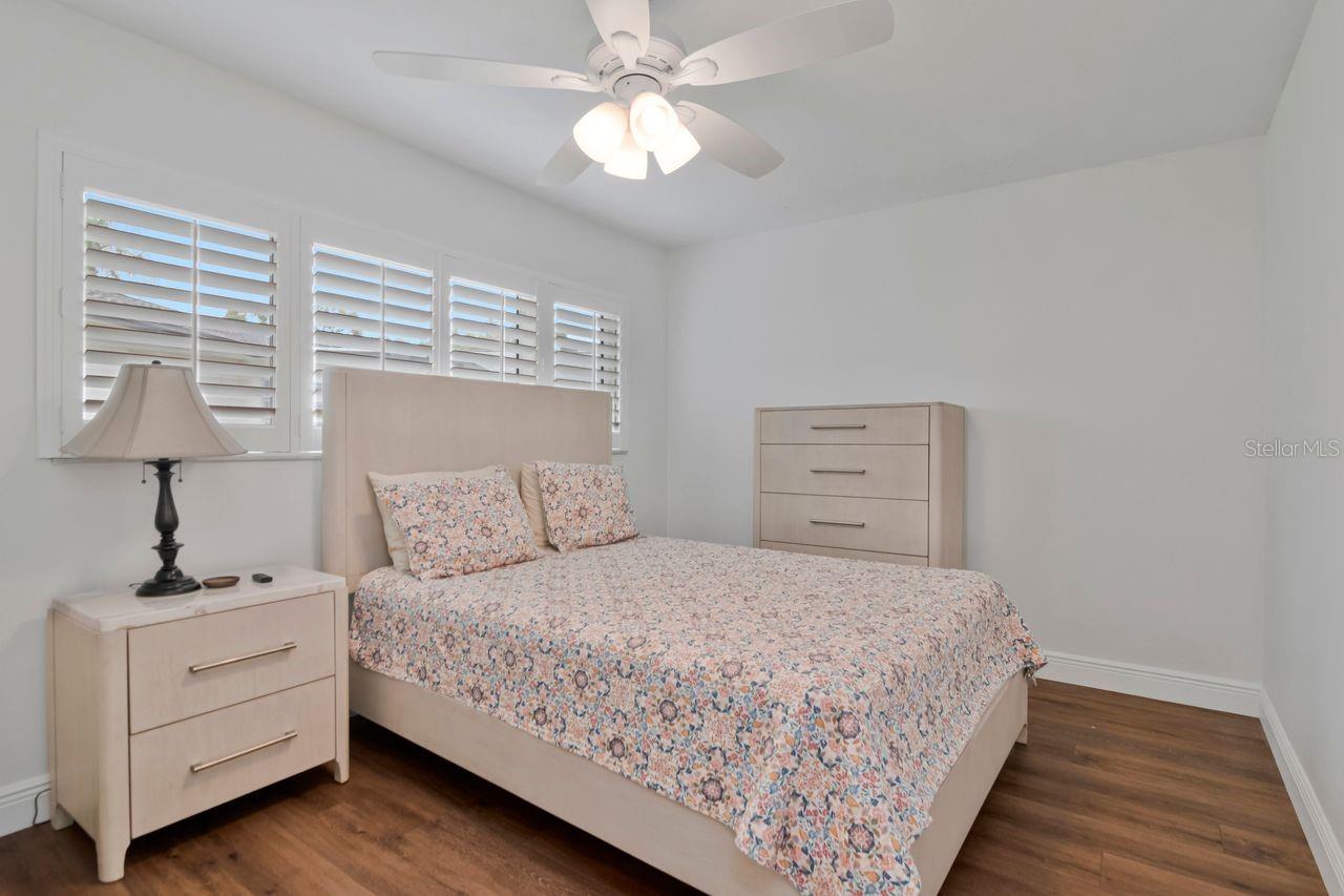 Bedroom with floral bedding, plantation shutters, and dark wood flooring.