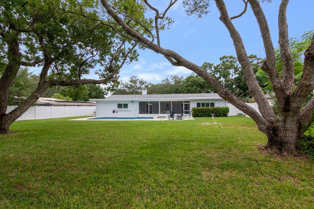 Single-story white home with a backyard pool, patio seating, and large trees framing the lawn.