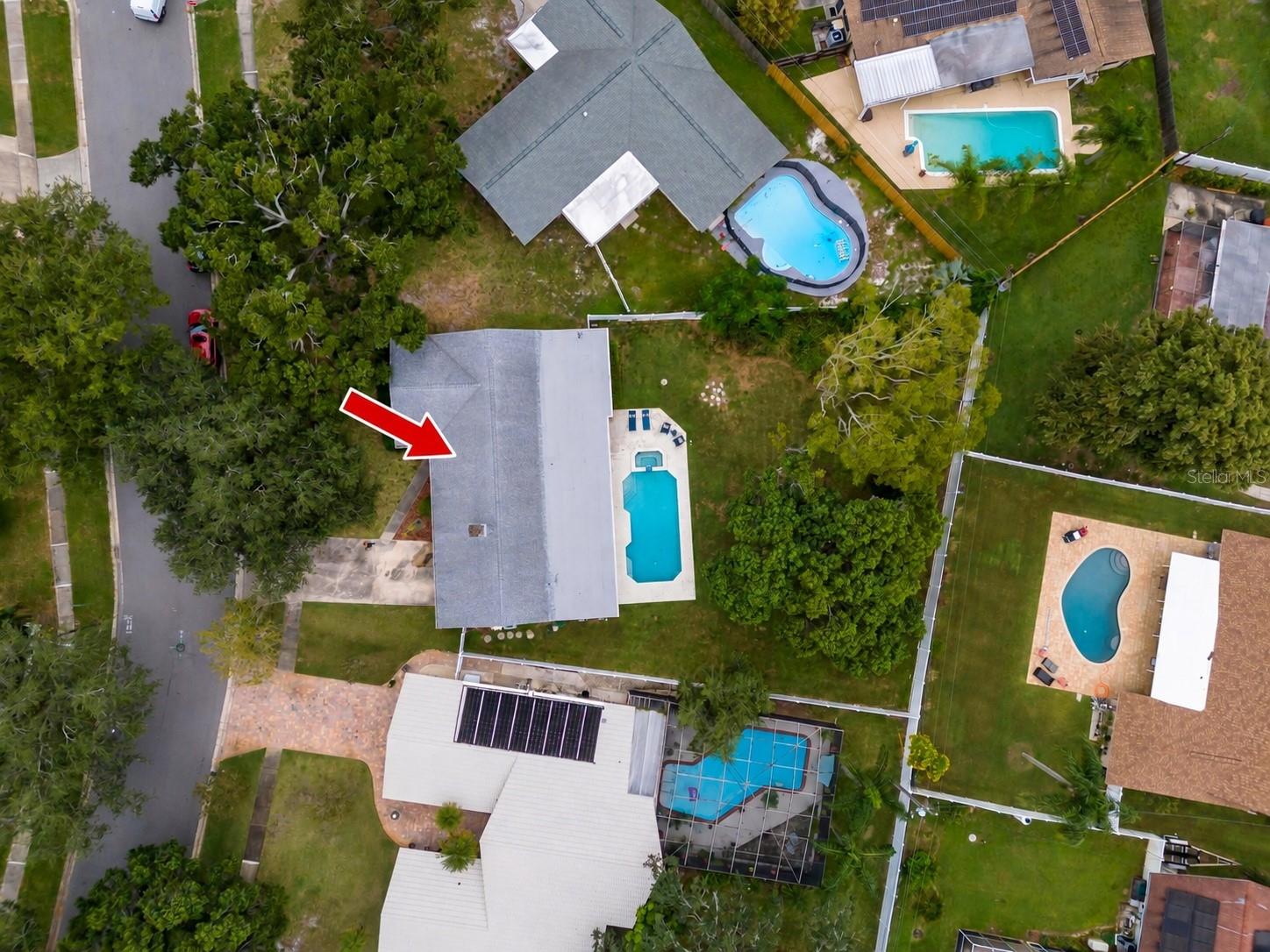 Aerial view of a gray-roofed home with a narrow pool, marked by a red arrow.