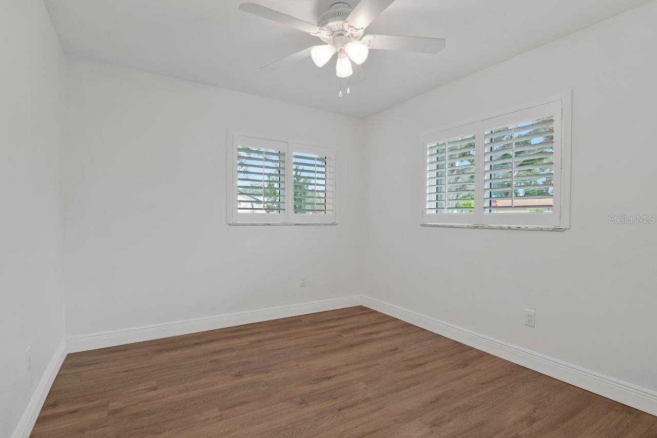 Empty room with wood-look flooring, shuttered windows, and a white ceiling fan with lights.