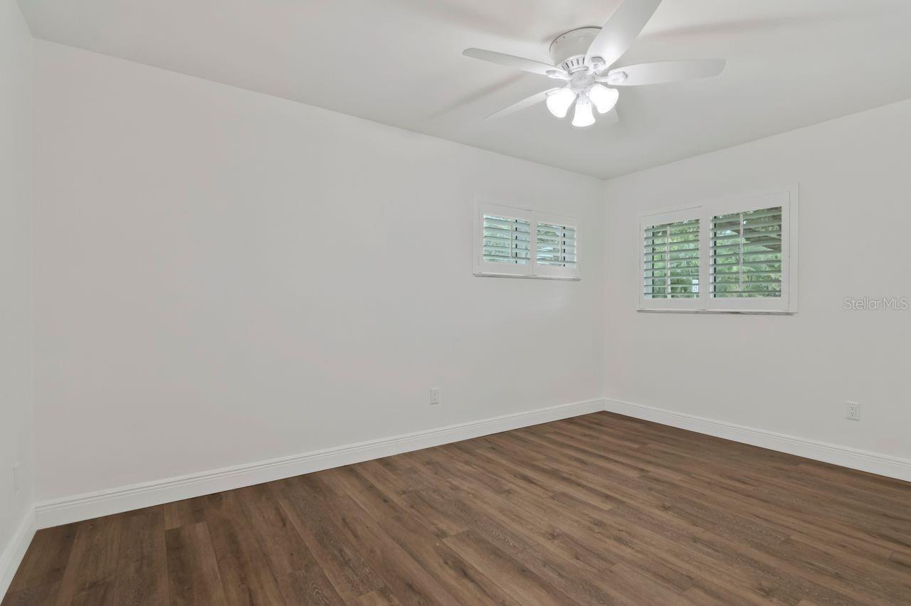 Empty room with wood-look flooring, two shuttered windows, and a ceiling fan.