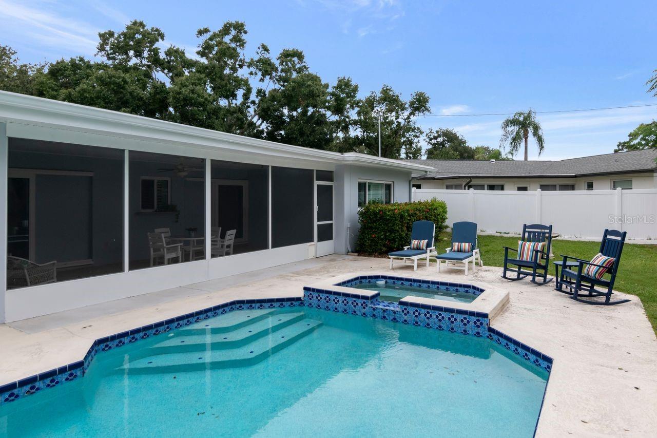 Backyard pool and raised spa beside a screened-in patio with outdoor seating.