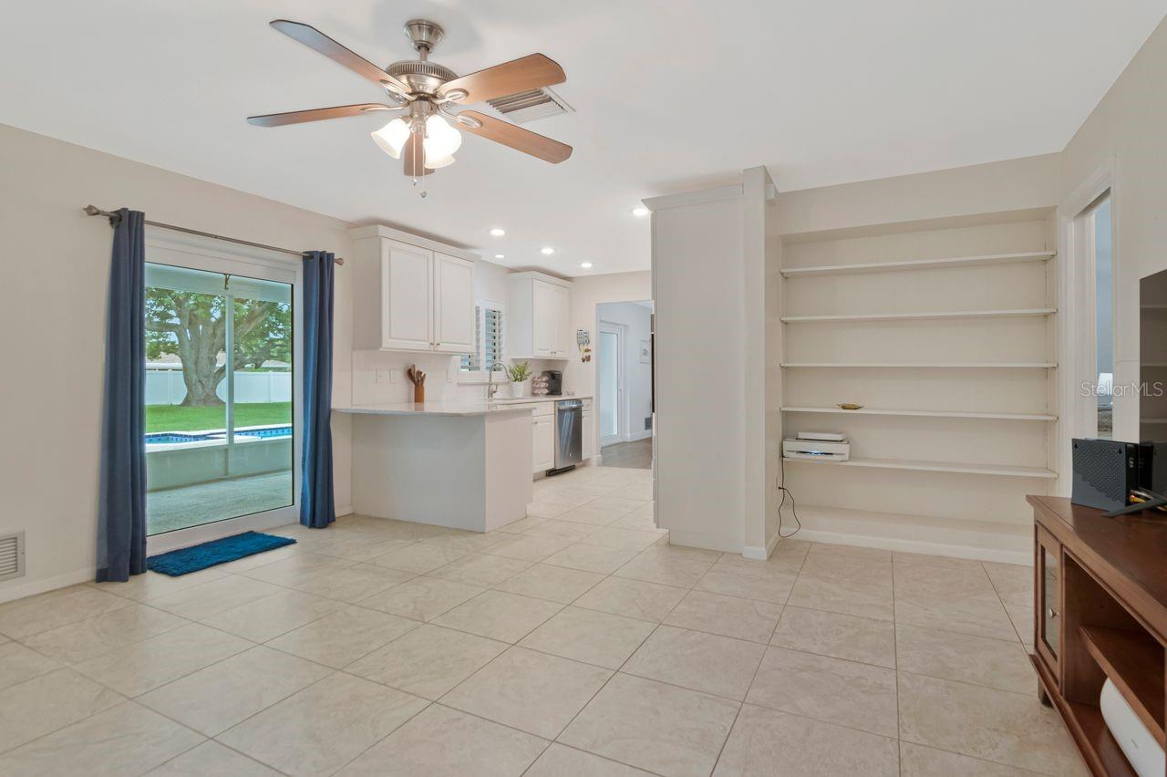 Open kitchen and living area with white cabinetry, built-in shelves, and sliding doors overlooking a pool.