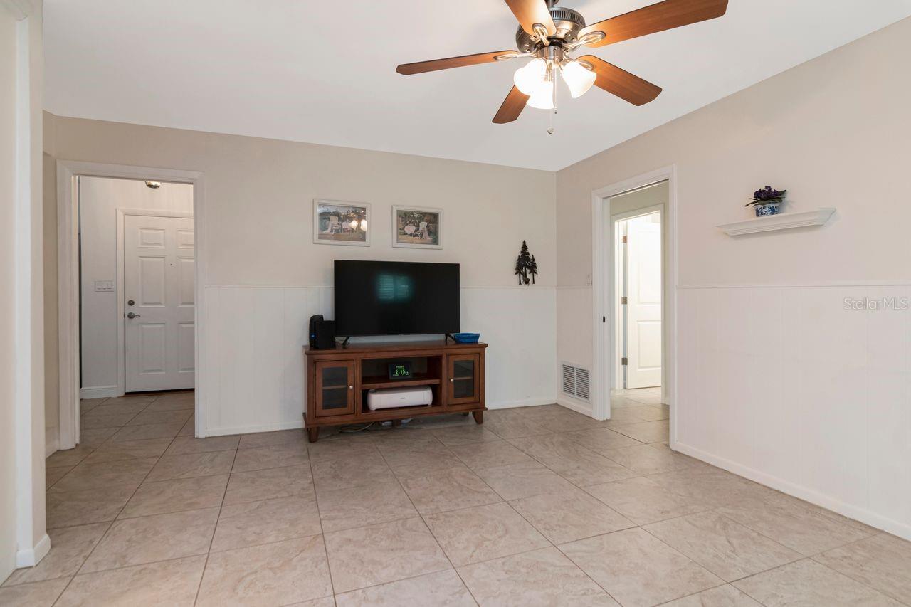 Living room with tiled floors, white wainscoting, and a ceiling fan above a television console.
