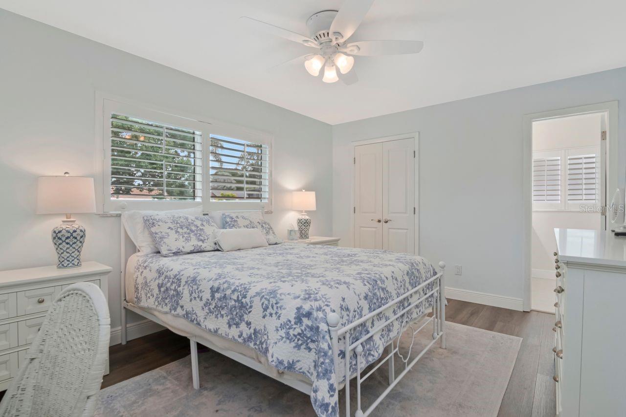 Bedroom with blue floral bedding, plantation shutters, and a white ceiling fan.