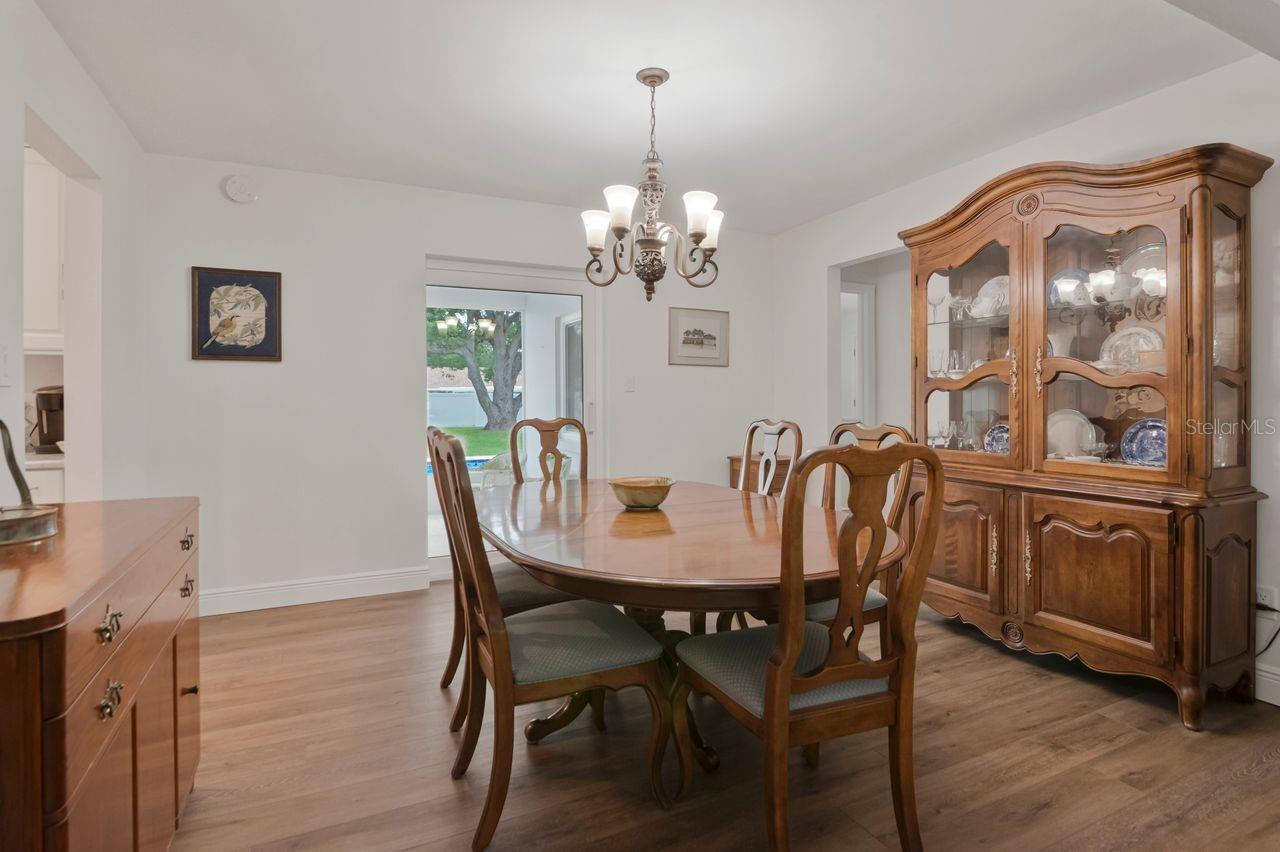 Dining room with a wooden table and china cabinet, chandelier, and sliding door overlooking the backyard pool.