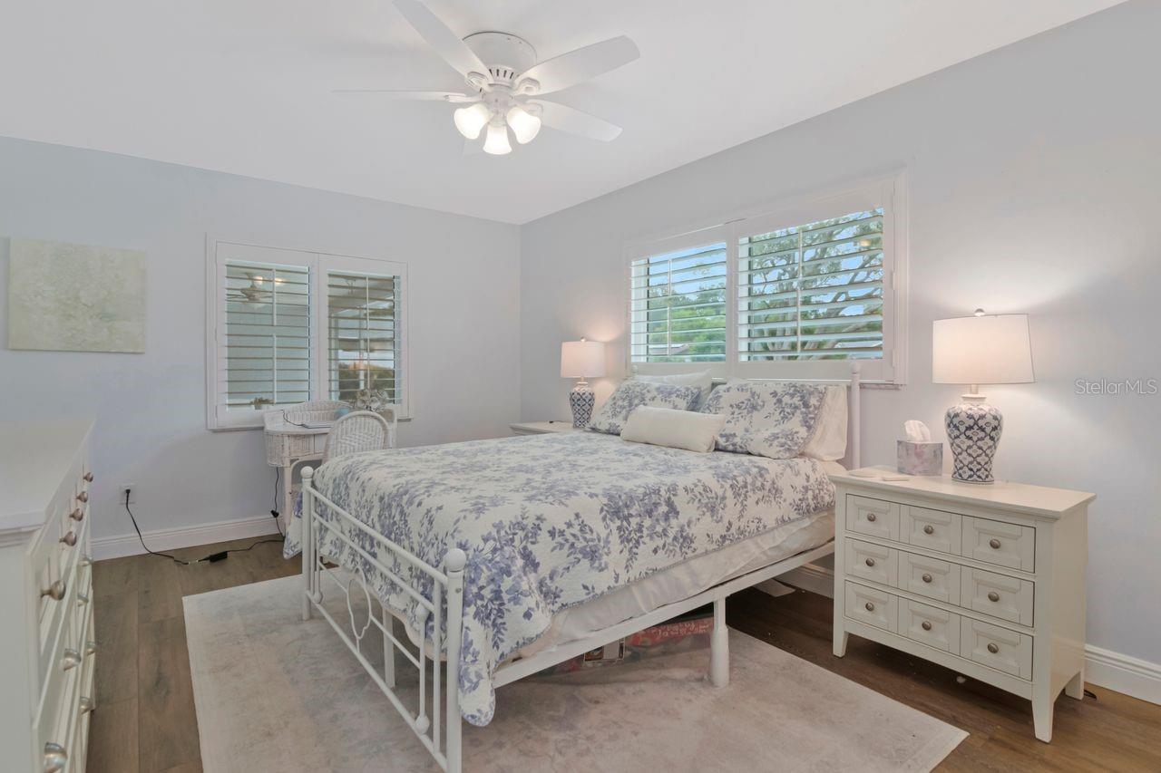 Bedroom with blue floral bedding, plantation shutters, and white bedside furniture.