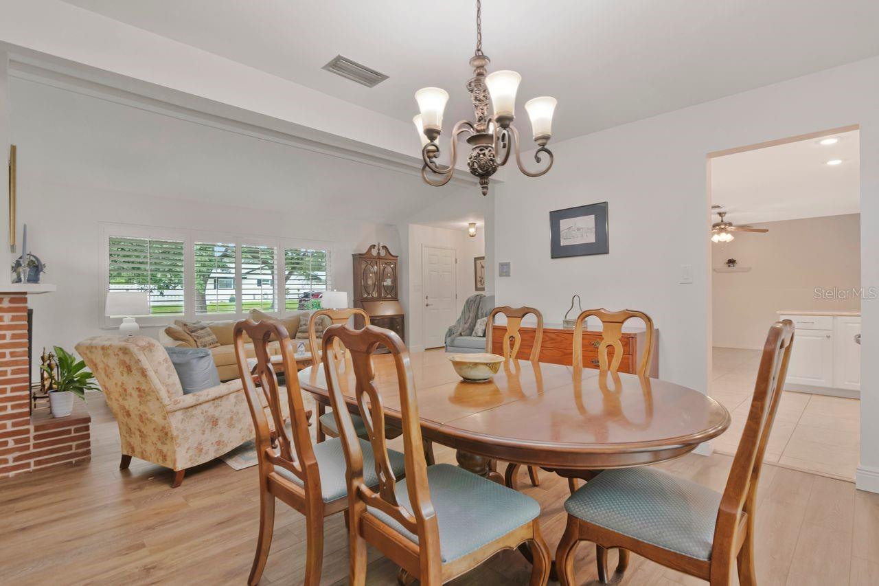 Furnished dining room with an oval wooden table, matching chairs, and chandelier beside a living area.