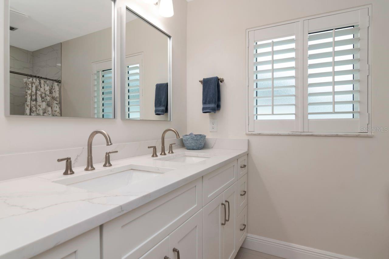 Bathroom with a white double vanity, marble-look countertop, and plantation shutters.