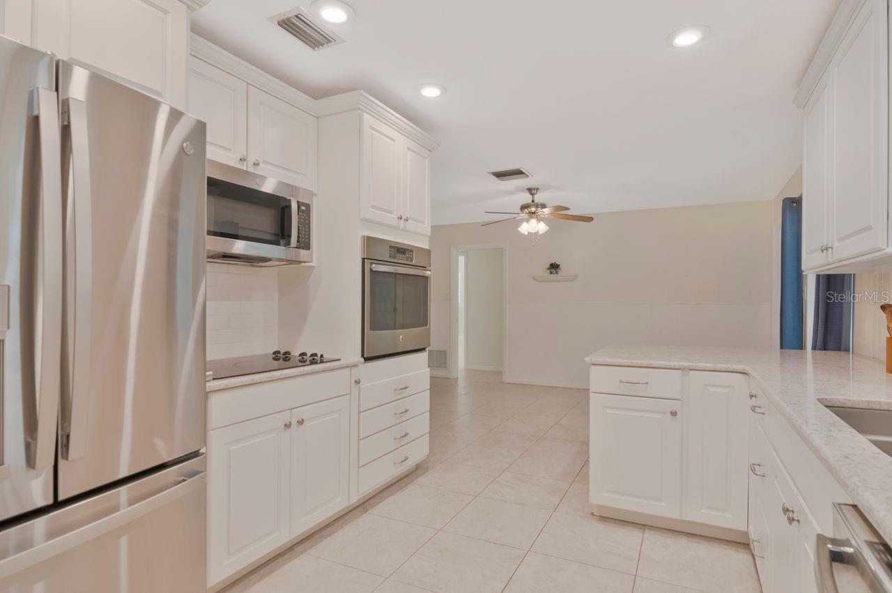 White kitchen with stainless steel appliances, a large island, and light tile floors.