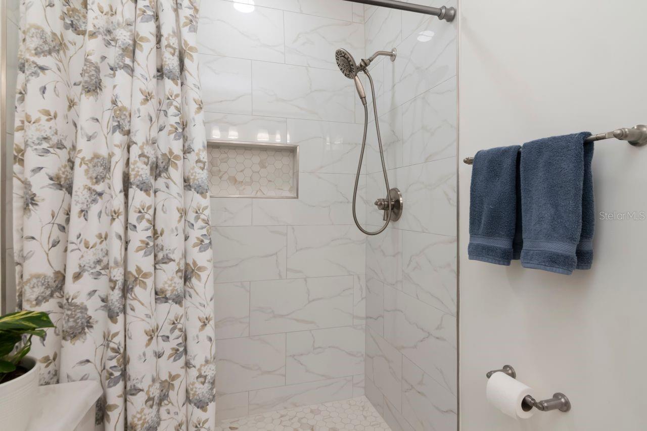 Bathroom shower with marble-look tile, a recessed hexagonal-tile niche, and floral curtain.