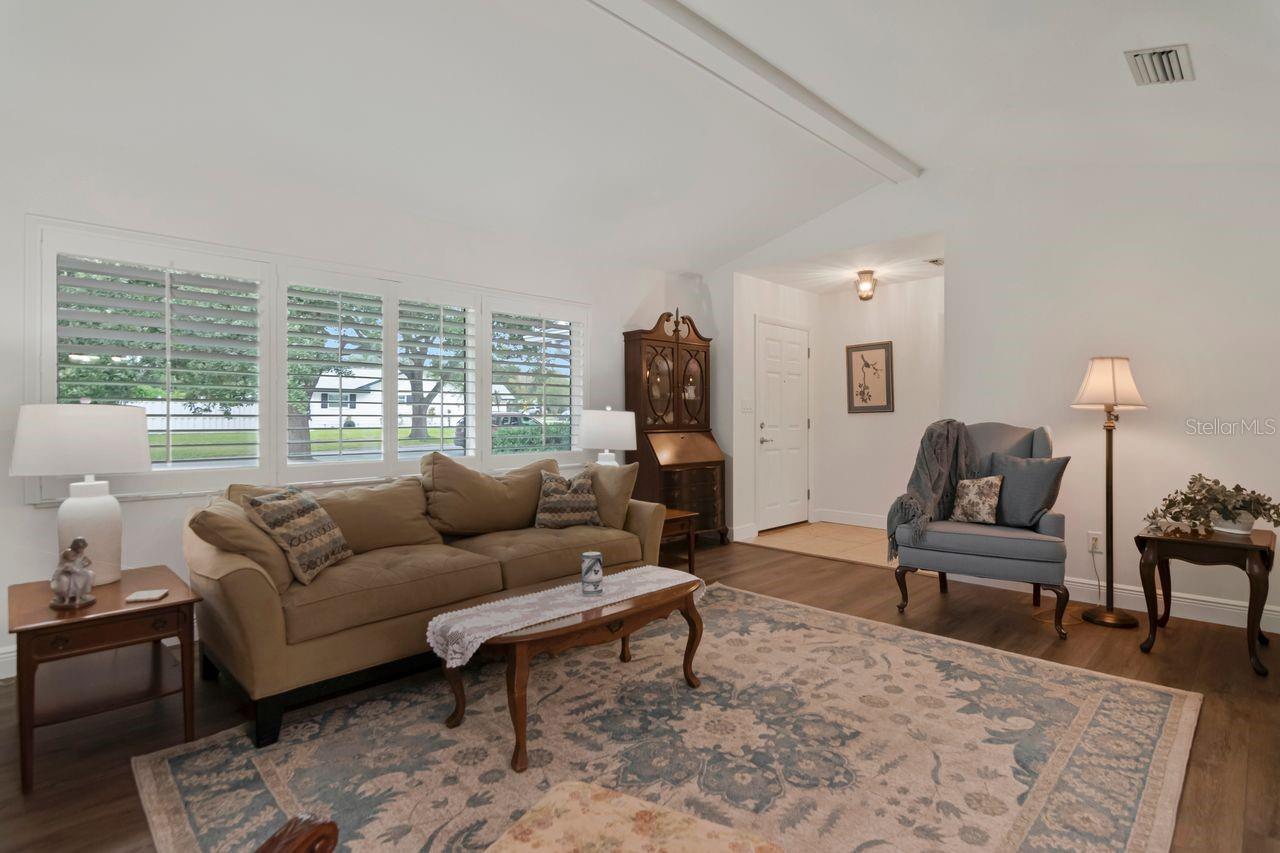 Living room with a tan sofa, blue-gray armchair, and wide shuttered windows.