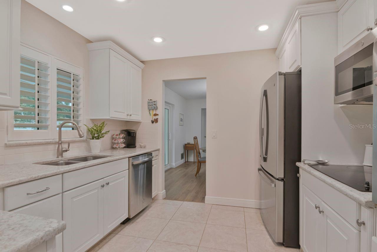 Kitchen with white shaker cabinets, stone counters, stainless appliances, and plantation shutters.