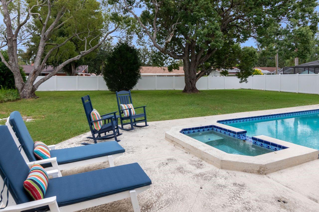 Backyard pool and built-in spa beside blue-cushioned lounge chairs and a white privacy fence.