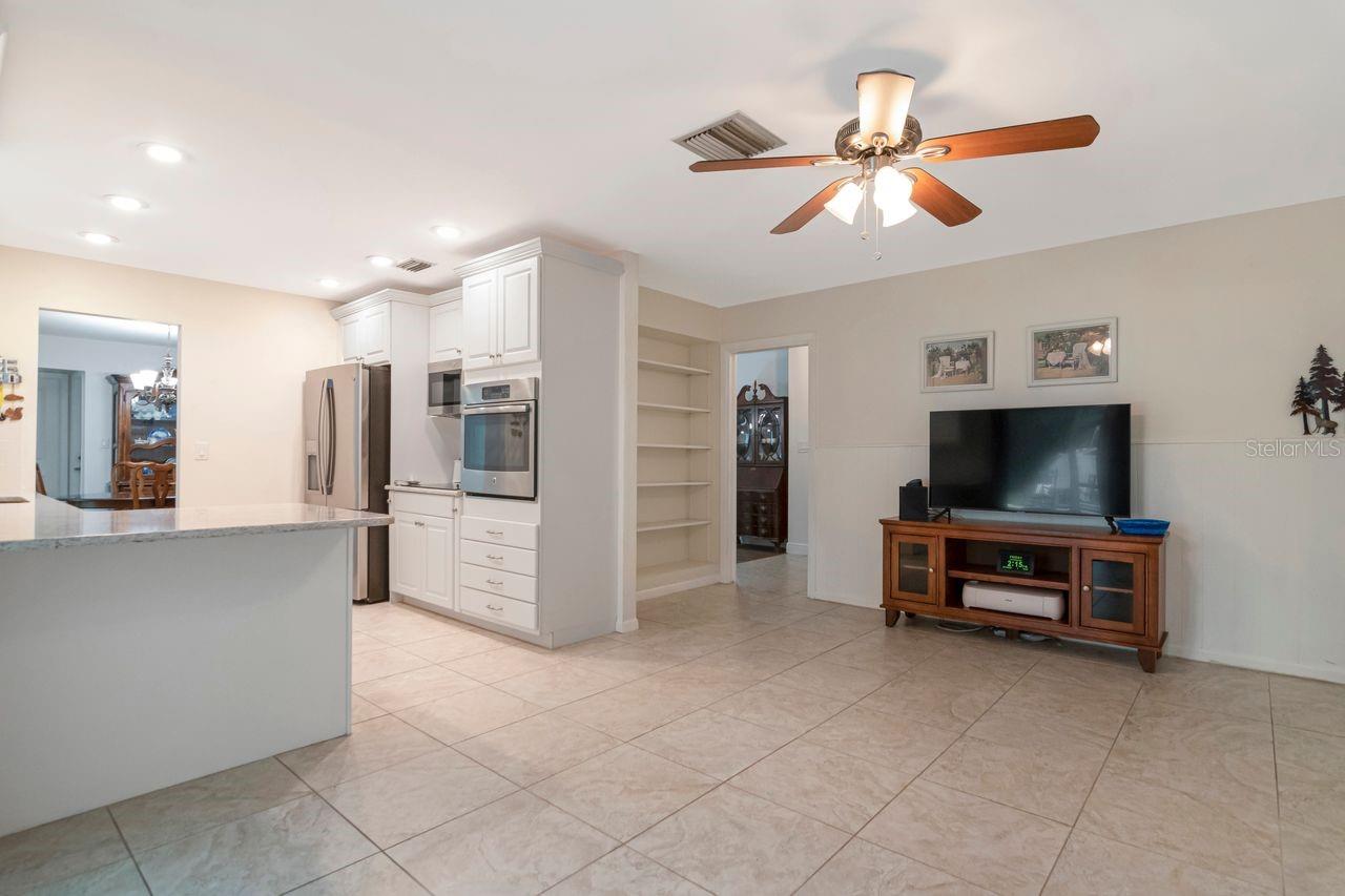 Kitchen and living area with white cabinets, a breakfast bar, tiled floors, and a ceiling fan.