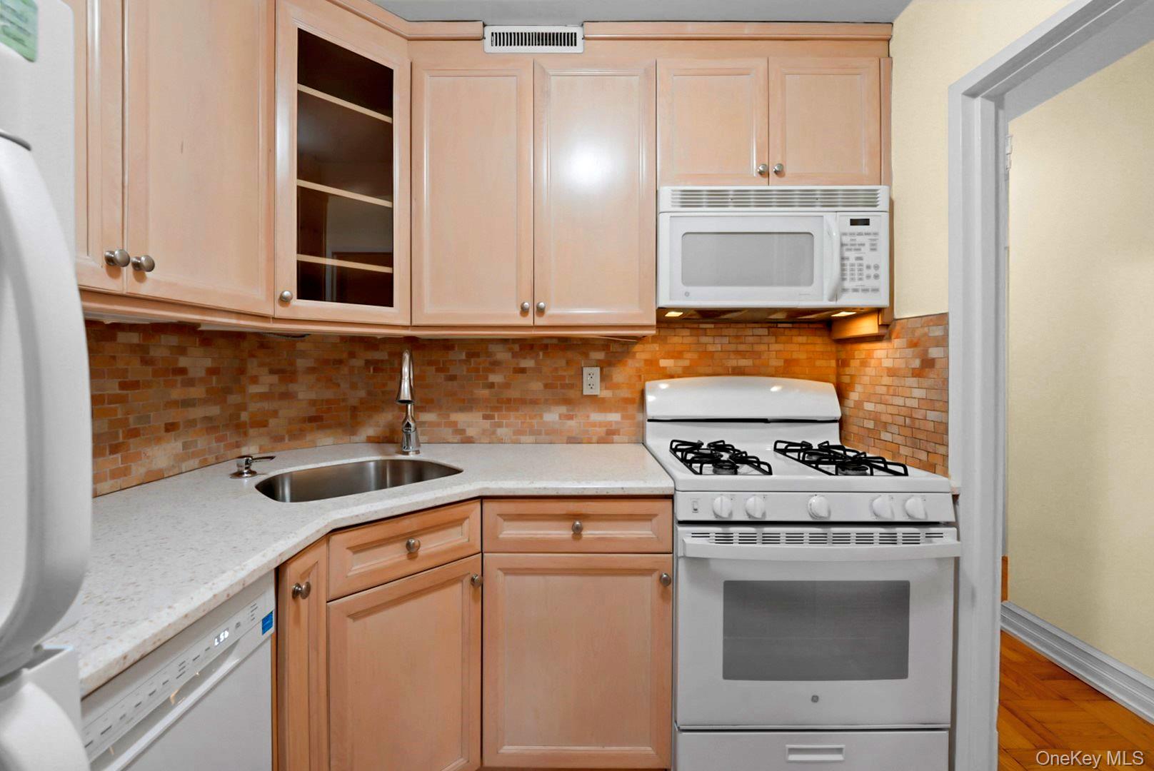 Kitchen with light wood cabinets, a tile backsplash, and a white gas range with overhead microwave.