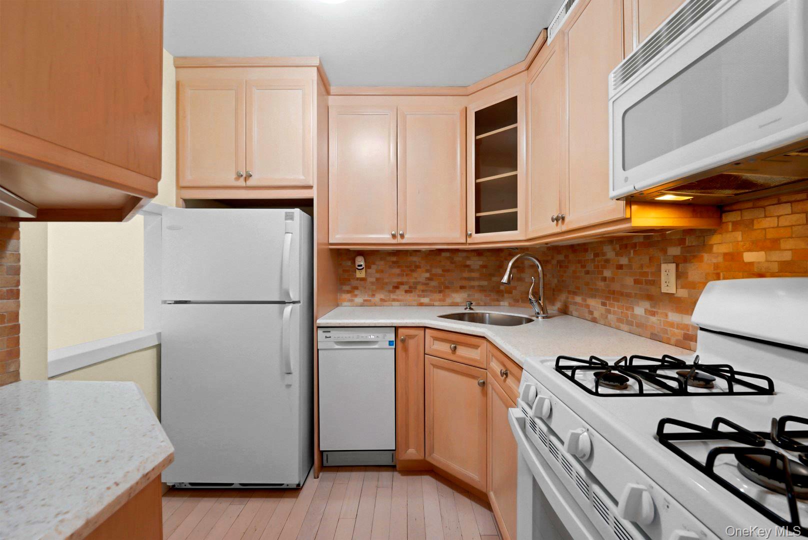 Compact kitchen with peach-toned cabinets, brick-pattern backsplash, and white appliances.