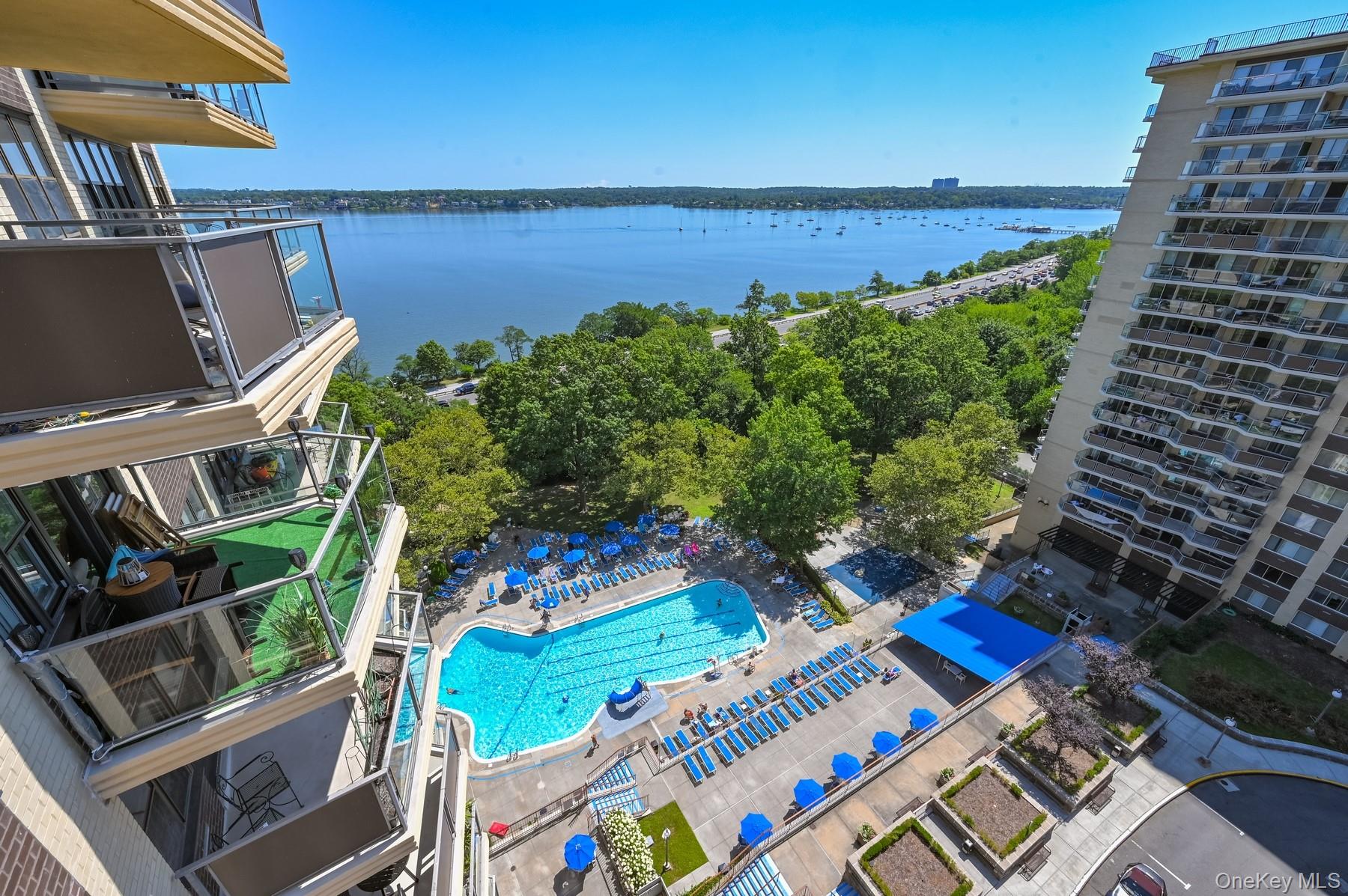 High-rise balcony overlooks a swimming pool, landscaped grounds, and a boat-dotted bay.