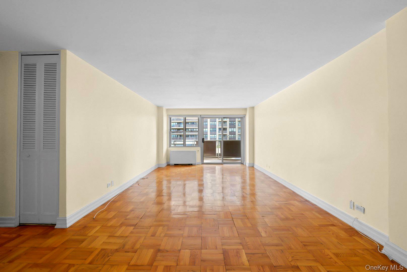 Vacant living room with parquet floors and sliding glass doors opening to a balcony.