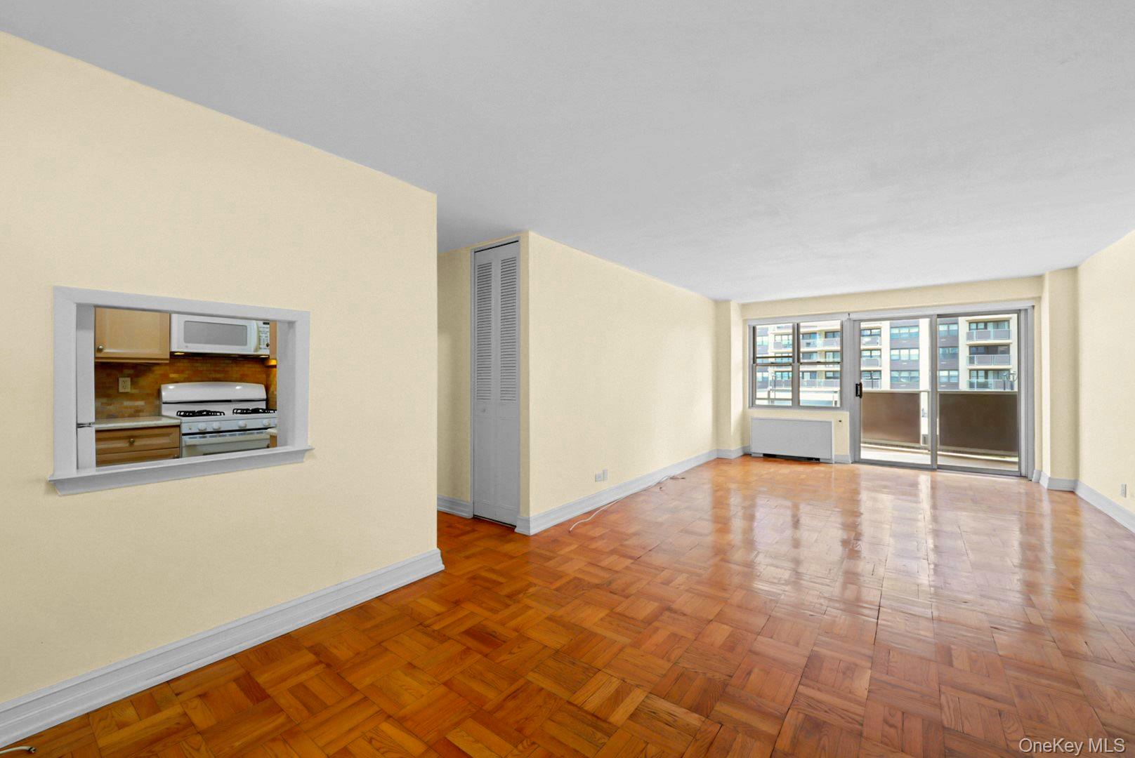 Vacant living room with parquet floors, kitchen pass-through, and sliding doors to a balcony.
