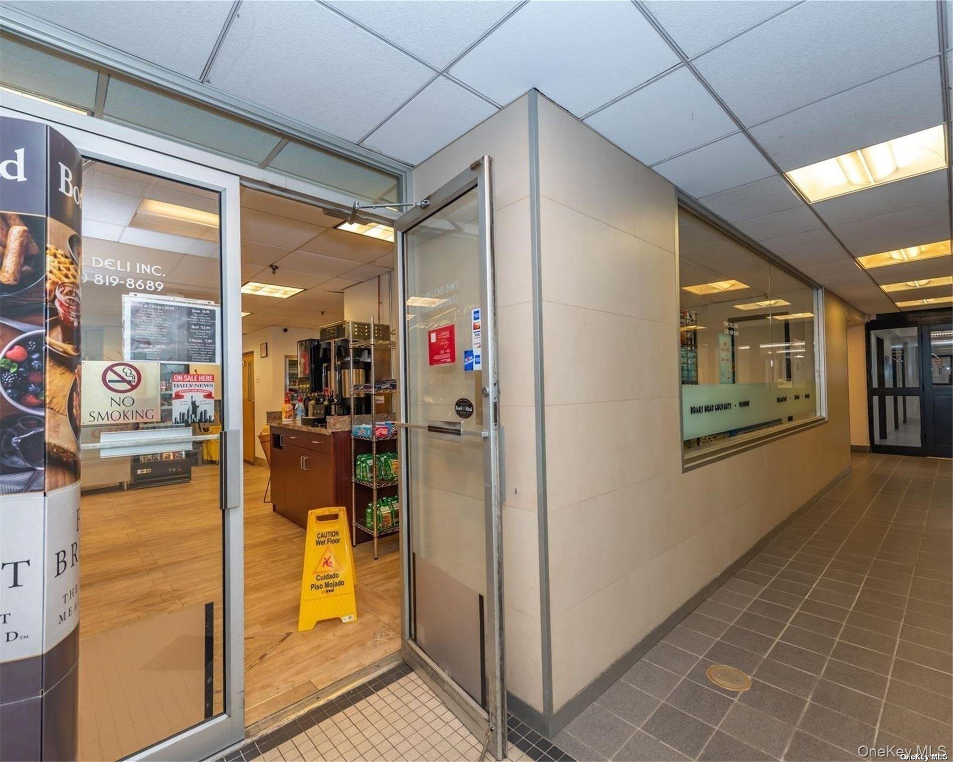 Deli storefront with an open glass door, service counter, snack shelves, and wet-floor sign.