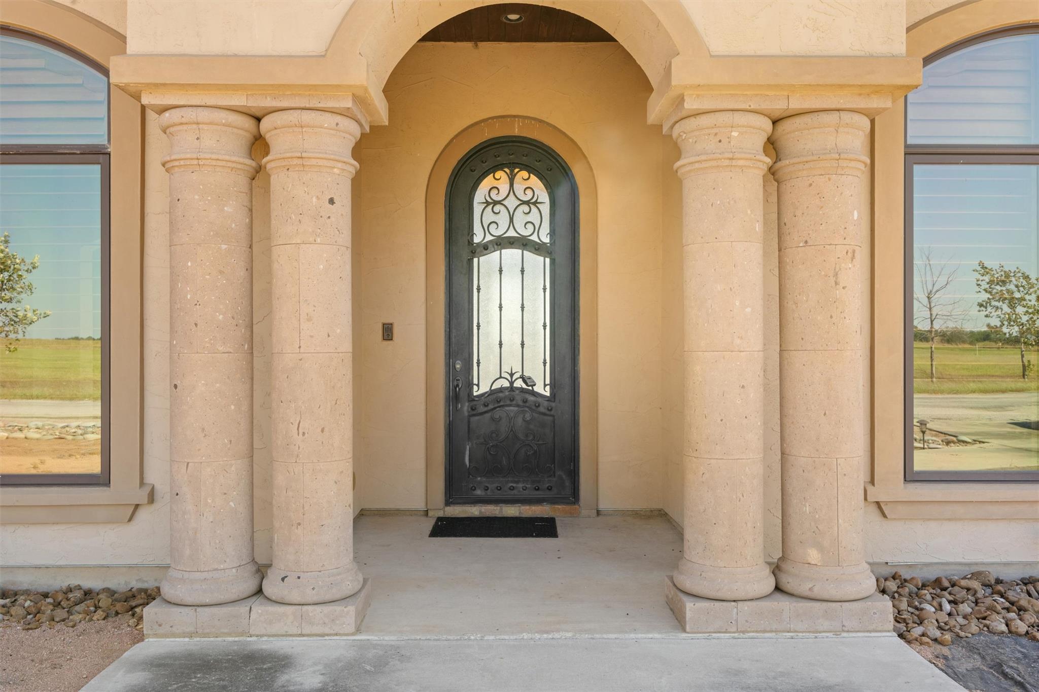 Home entrance with a wrought-iron door, arched portico, and paired stone columns.
