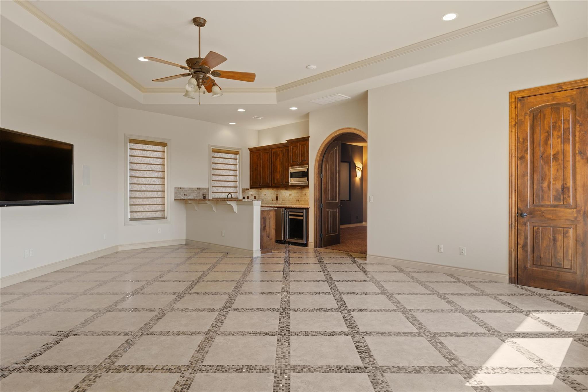 Empty living area with patterned tile floors, dark wood kitchen cabinets, and a wall-mounted television.