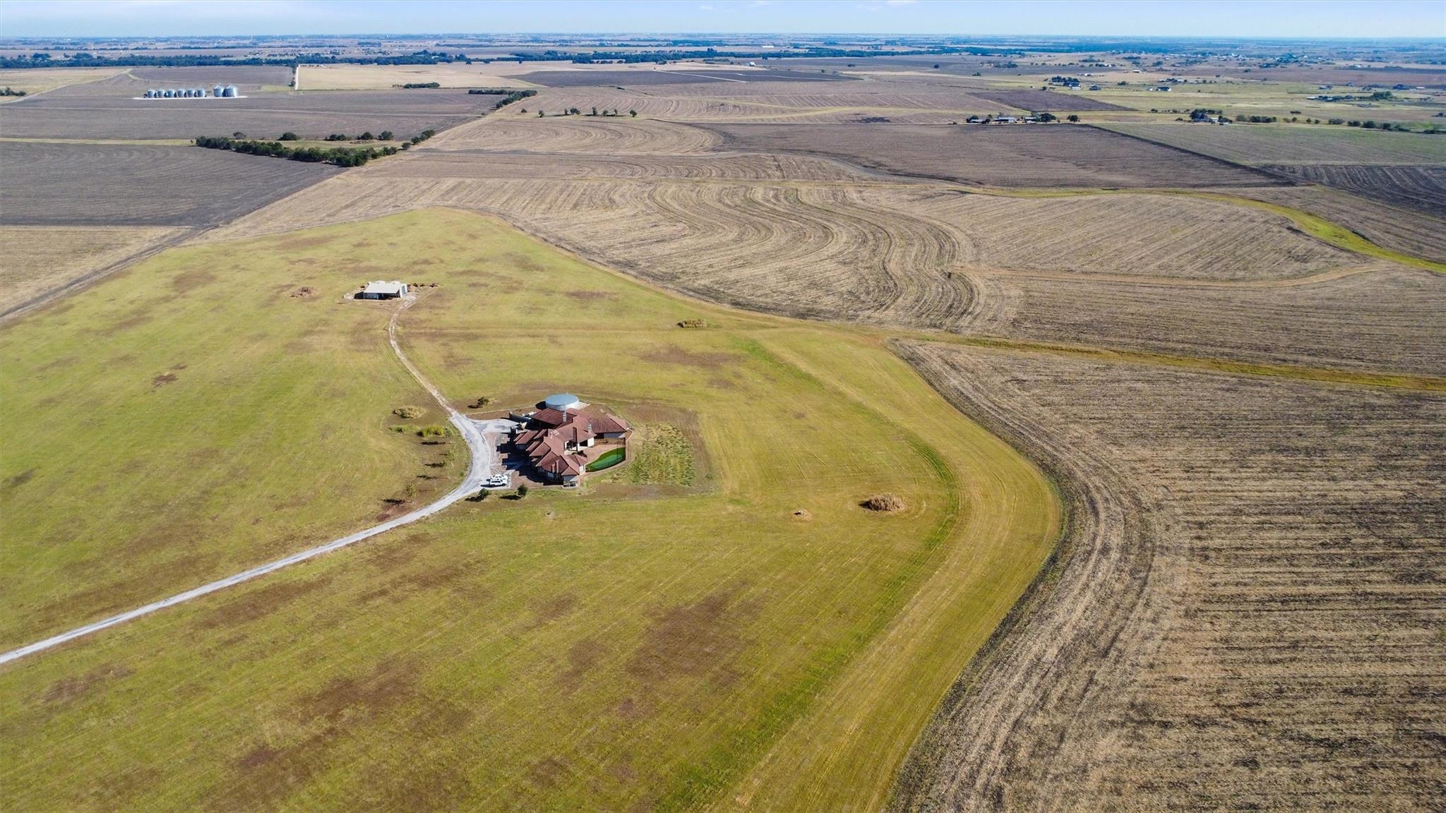 Aerial view of a rural home with a red roof and pool amid expansive fields.