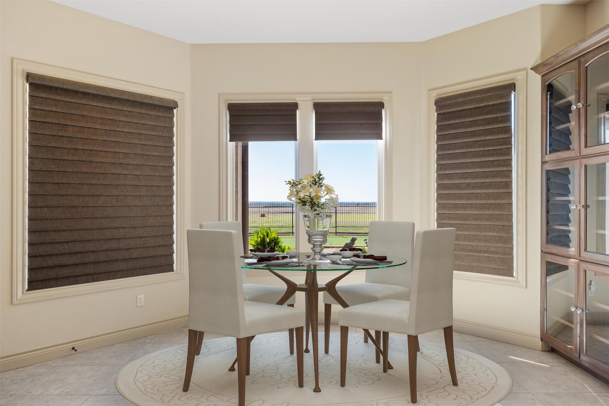 Dining room with a round glass table, upholstered chairs, and windows overlooking a fenced lawn.