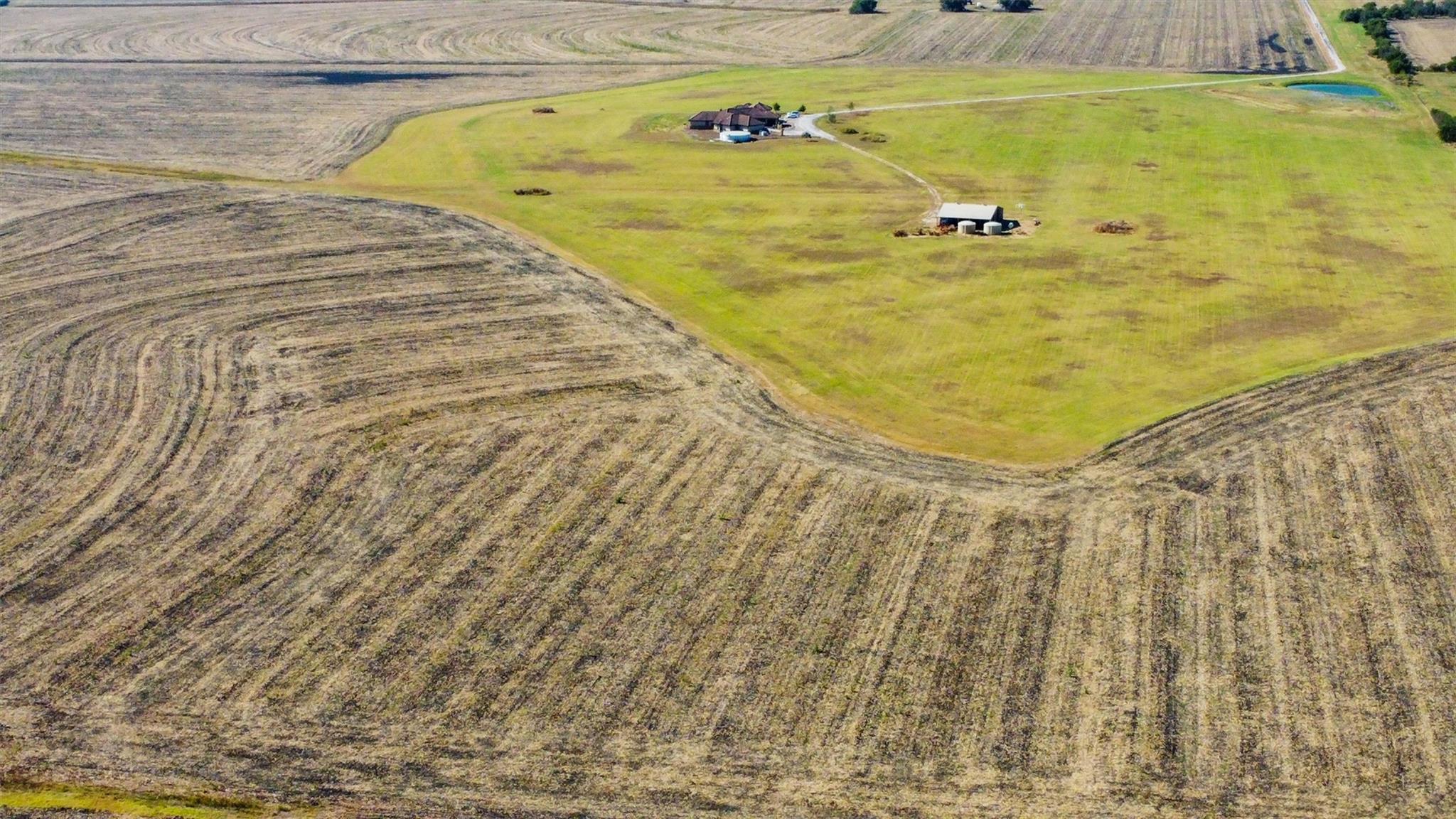 Aerial view of a rural home and outbuilding in a grassy clearing amid harvested fields.