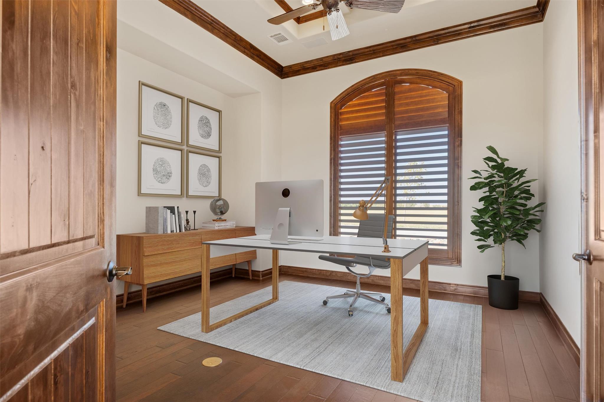 Home office with a wood desk, arched plantation shutters, and a coffered ceiling.