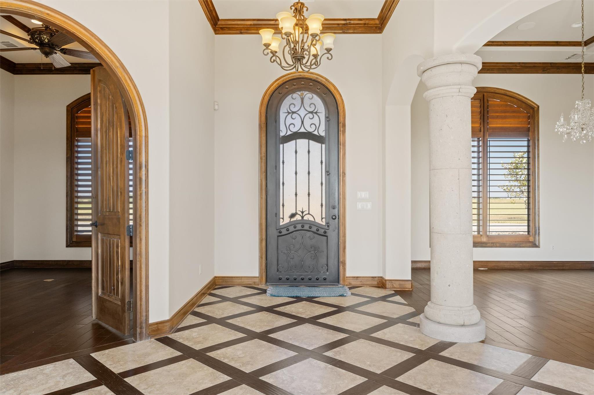 Foyer with an ornate iron front door, geometric tile floor, carved wood trim, and a stone column.