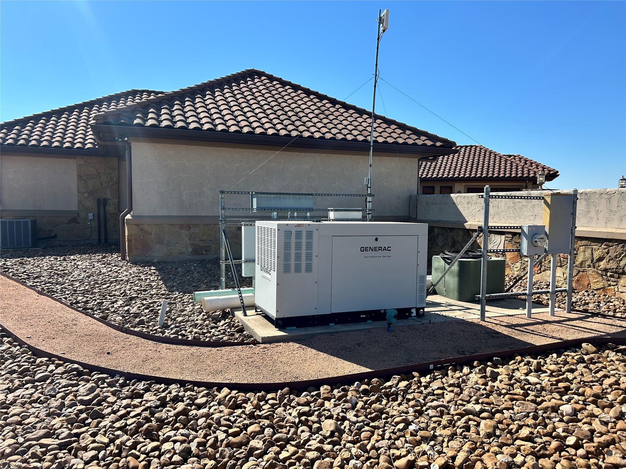 Standby generator beside a stucco home with a tiled roof and rock landscaping.