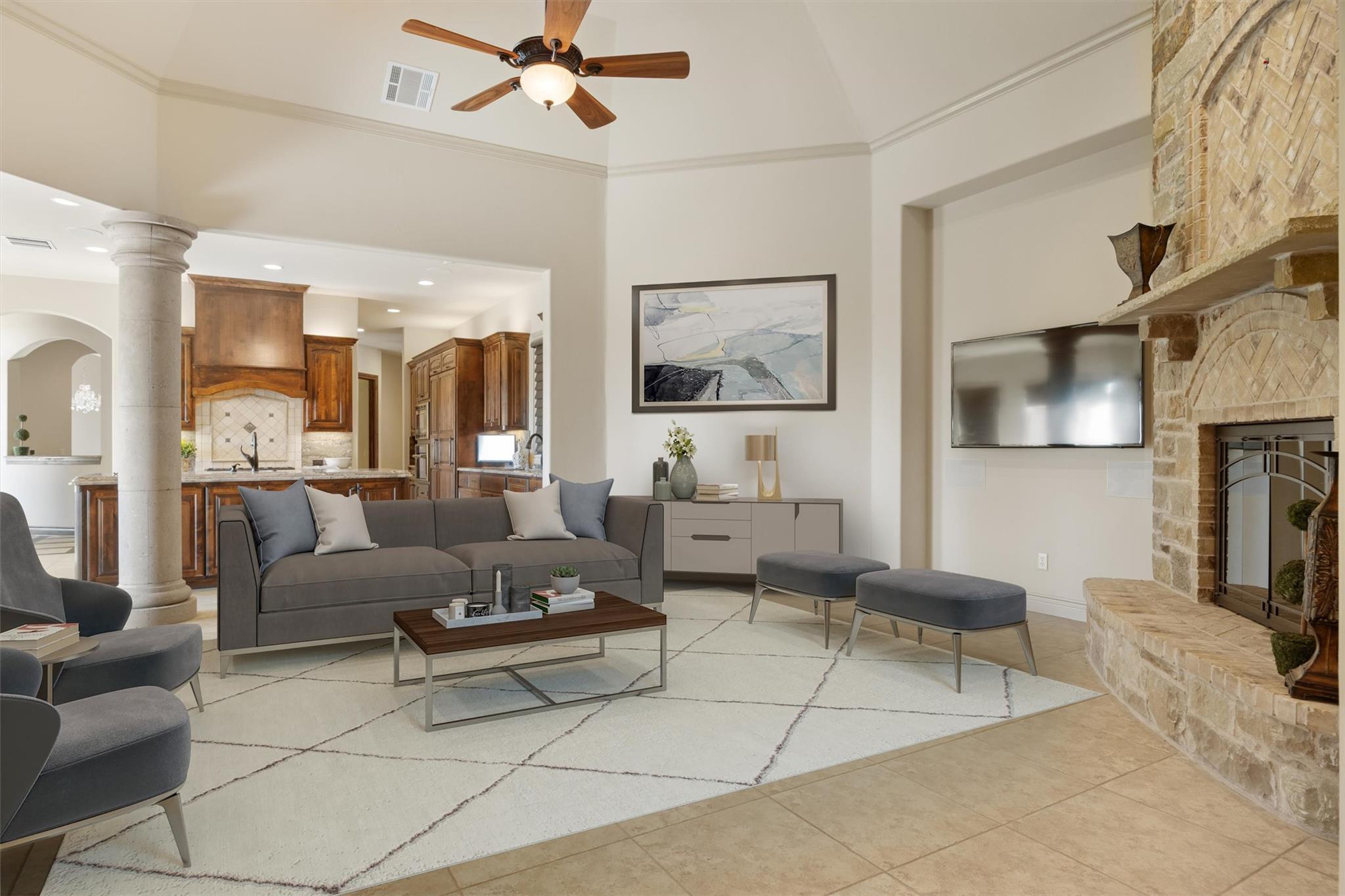 Open-plan living room with a stone fireplace, gray seating, and a wood-cabinet kitchen beyond.