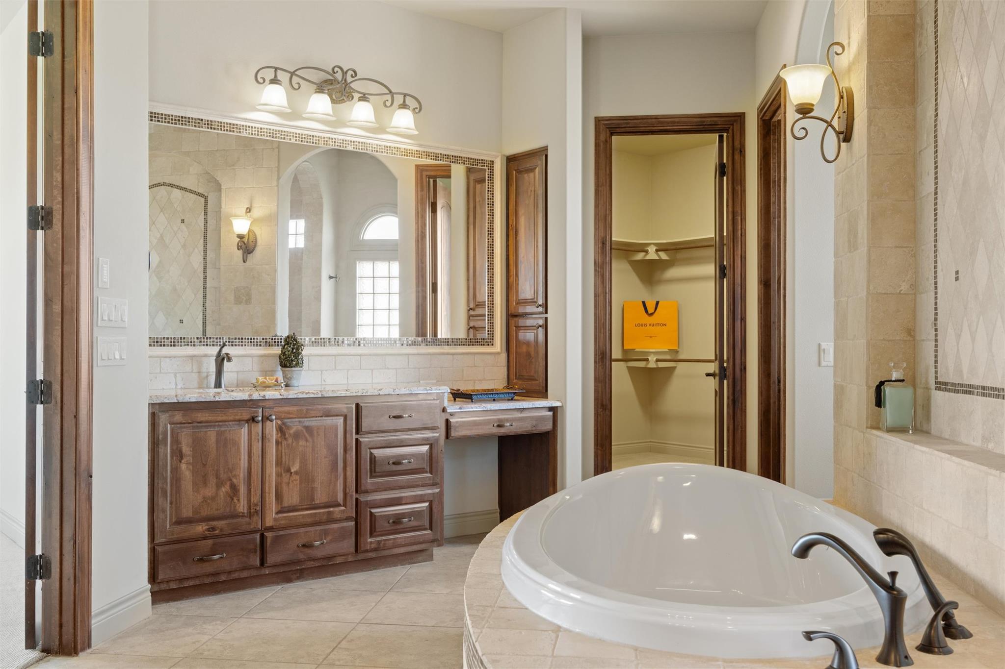 Bathroom with a large soaking tub, tiled shower, wood vanity, and open walk-in closet.