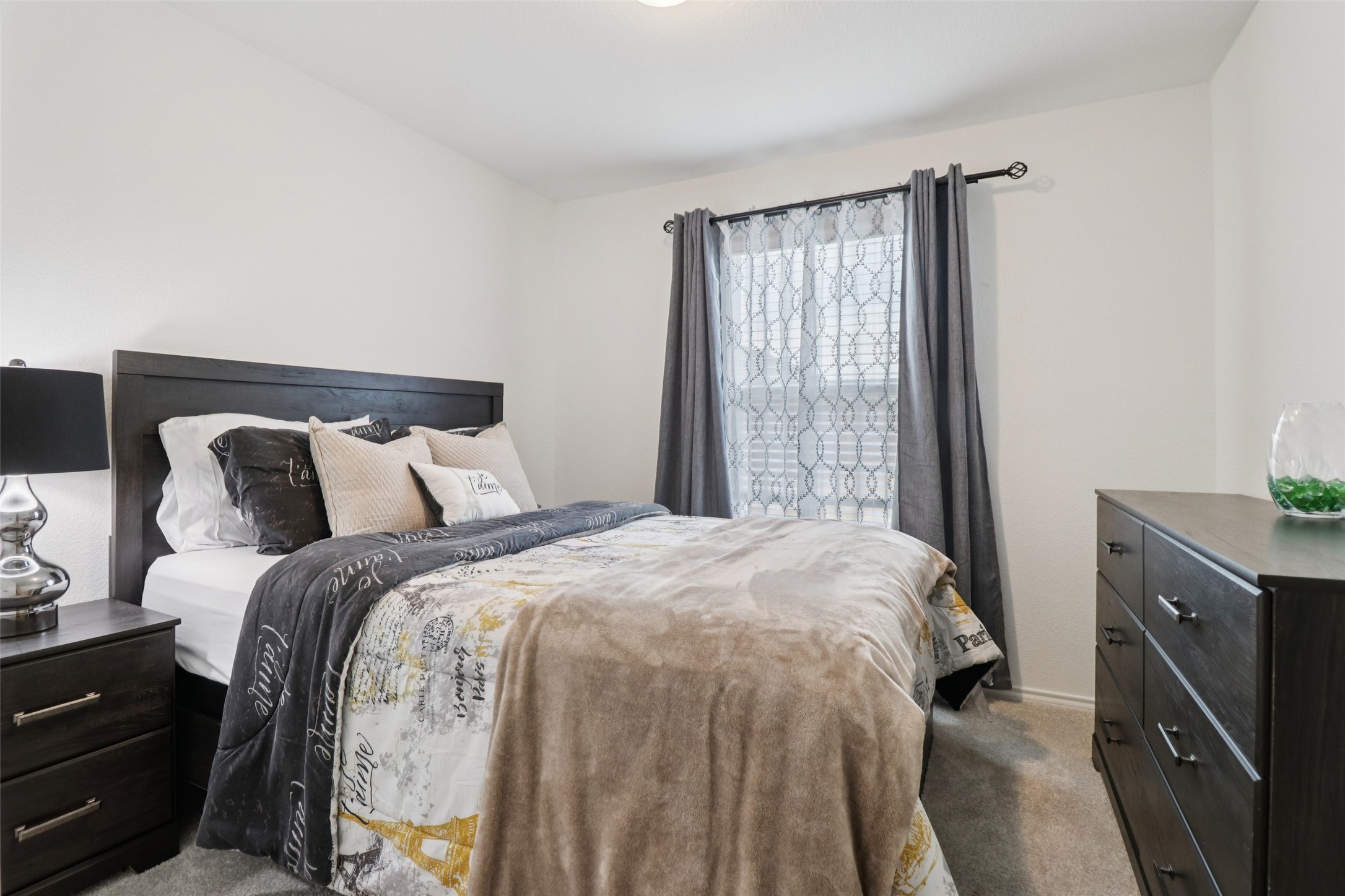 Furnished bedroom with a dark wood bed, layered neutral bedding, and gray curtains.
