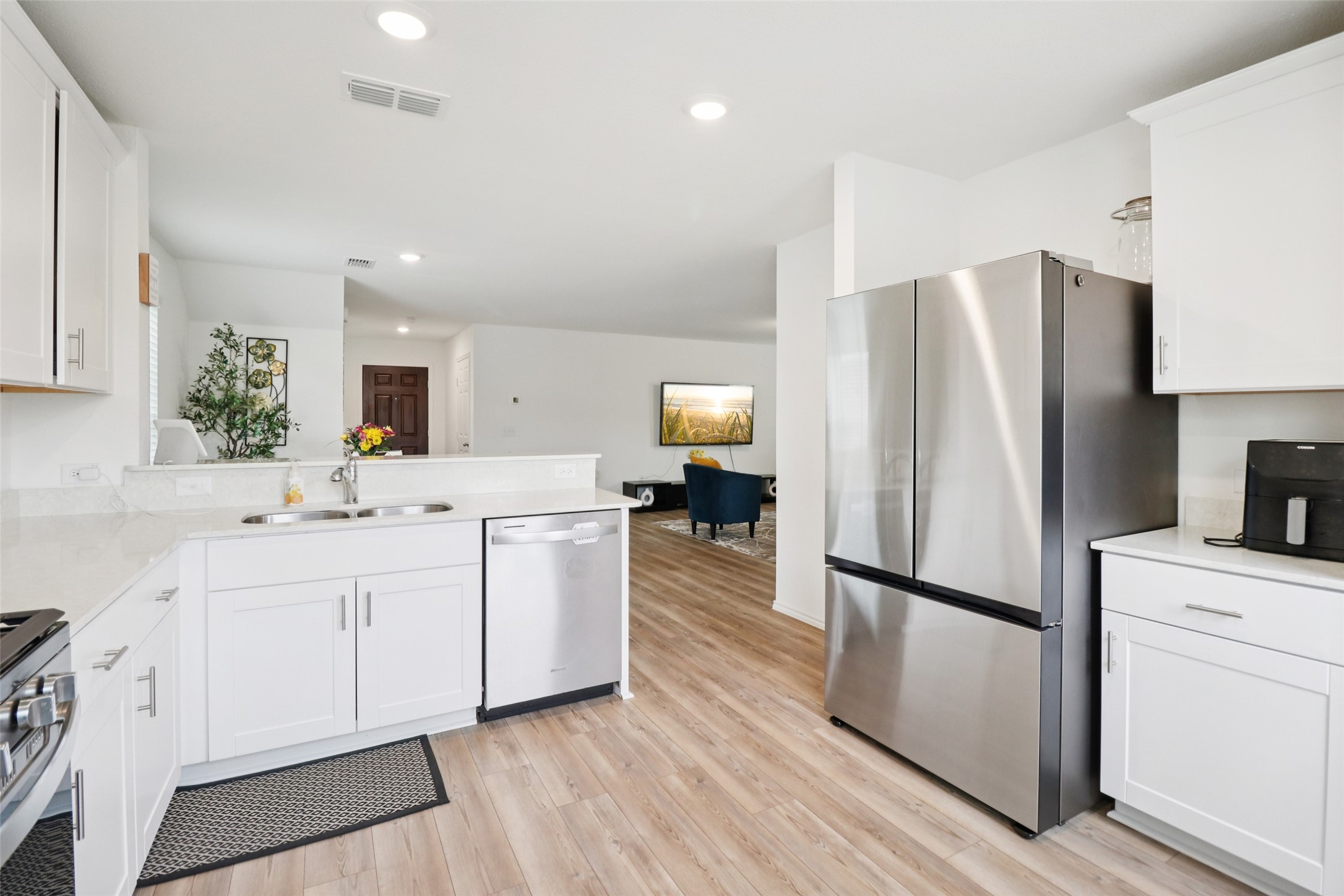 Bright white kitchen with stainless steel appliances and an open view into the living area.