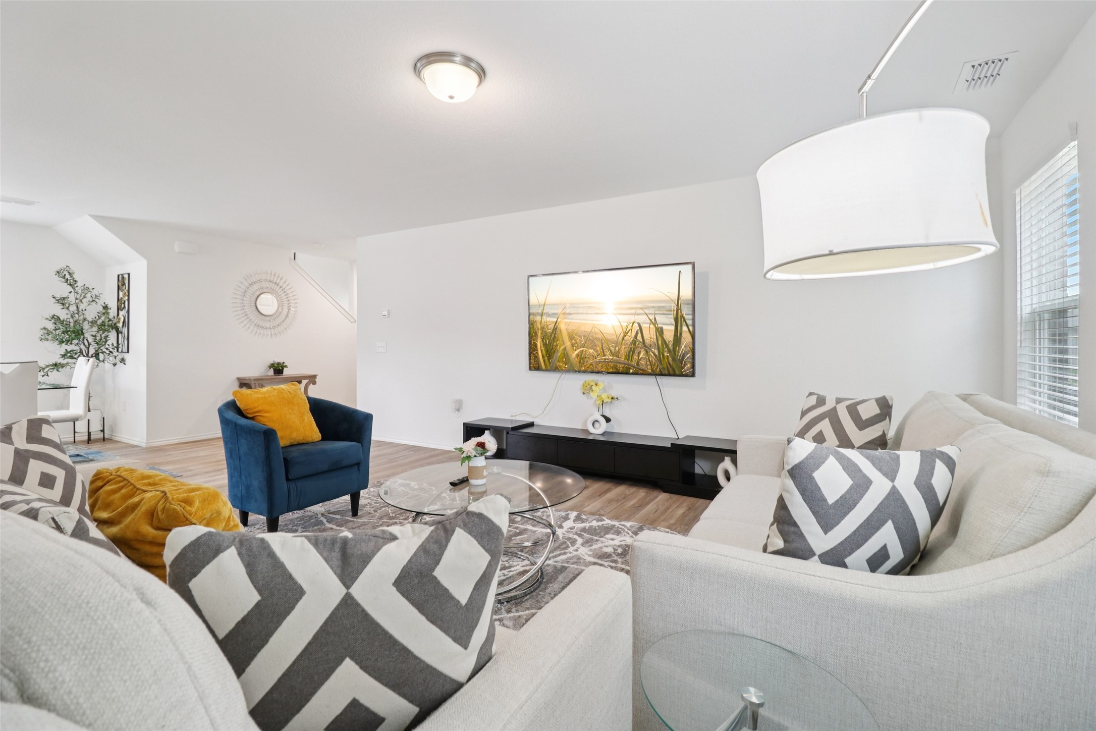 Staged living room with white sofas, geometric pillows, and a blue accent chair facing a wall-mounted television.