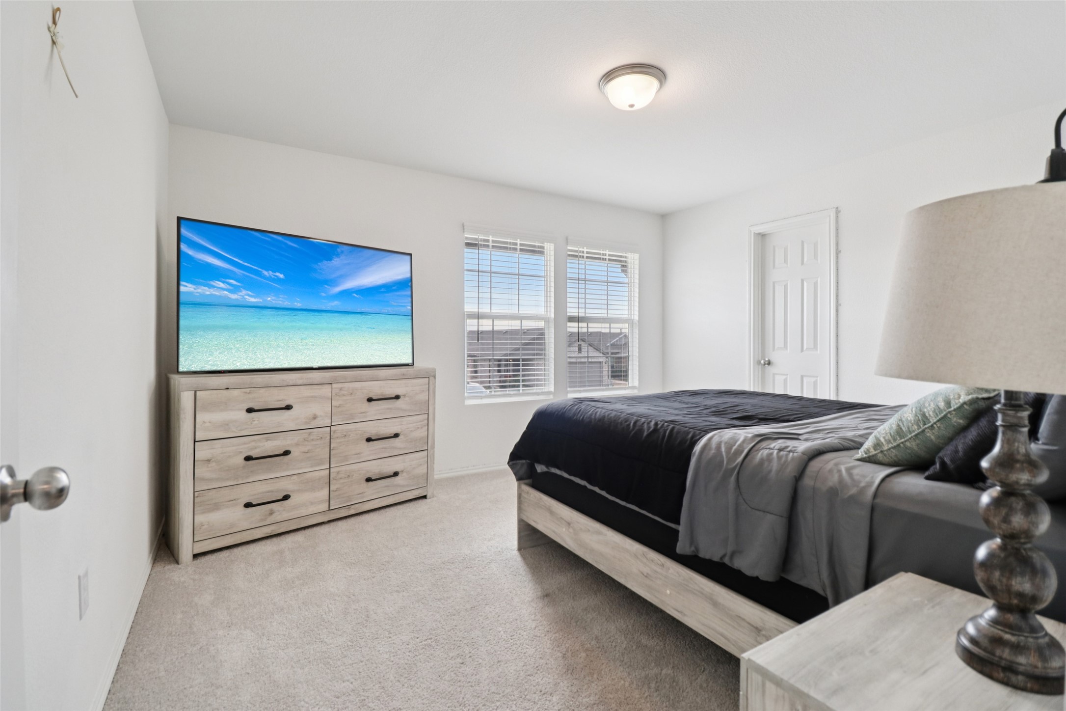 Bedroom with a large dark-bedded bed, light wood dresser, and television showing a beach.