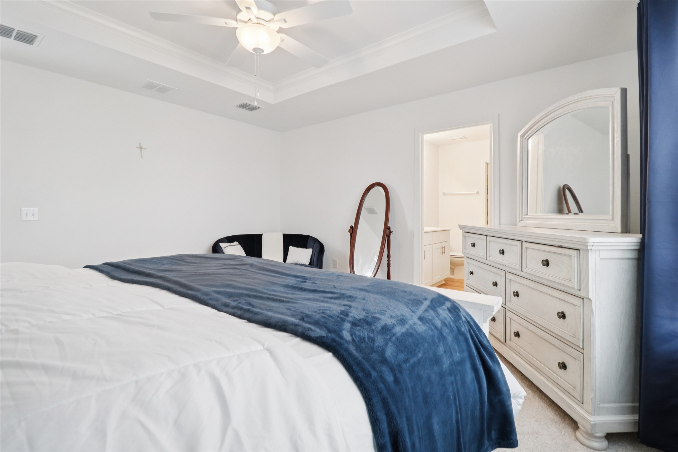 Bedroom with a navy throw on the bed, white dresser and arched mirror, and an adjoining bathroom doorway.