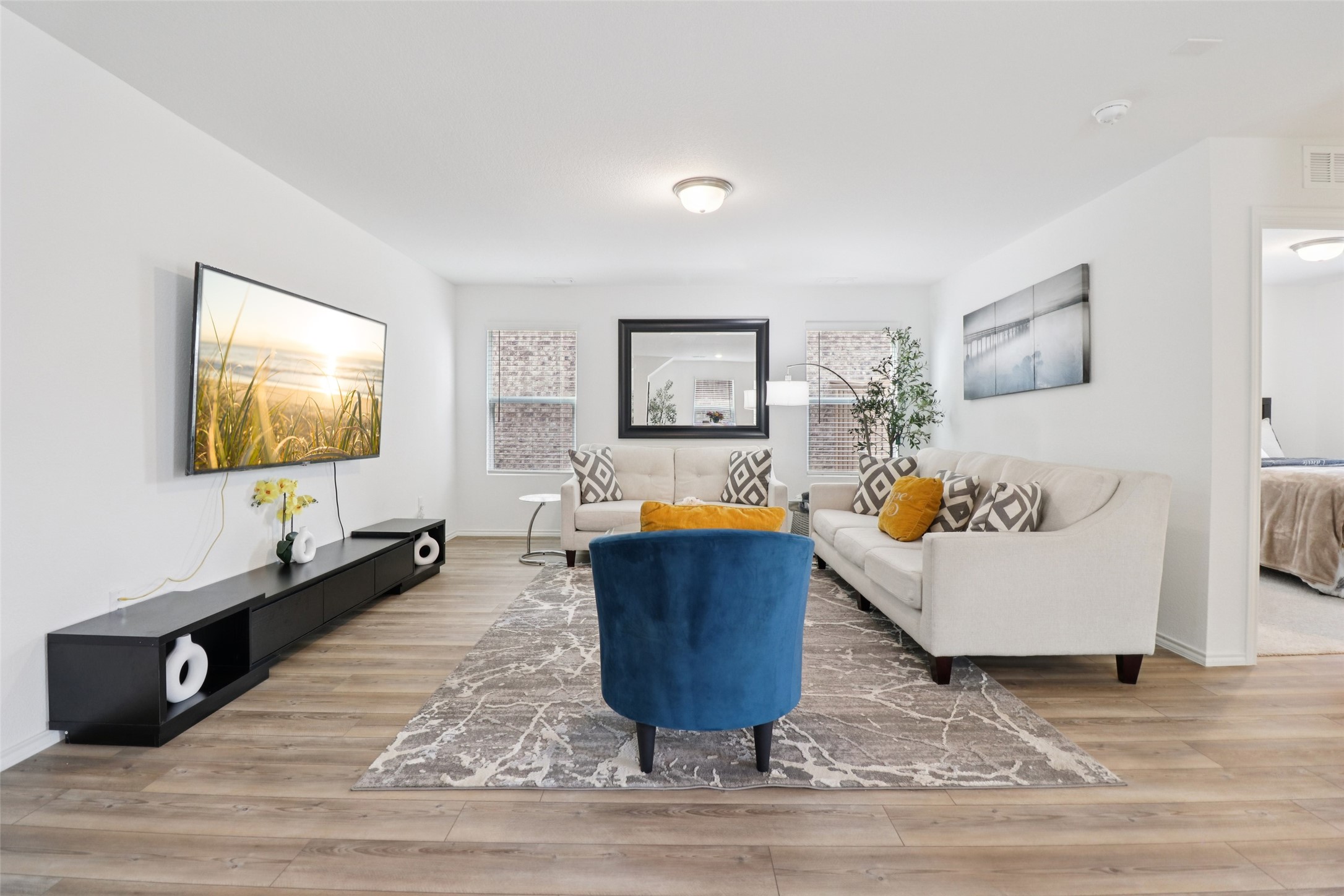 Staged living room with white sofas, a blue accent chair, and wood-look floors.