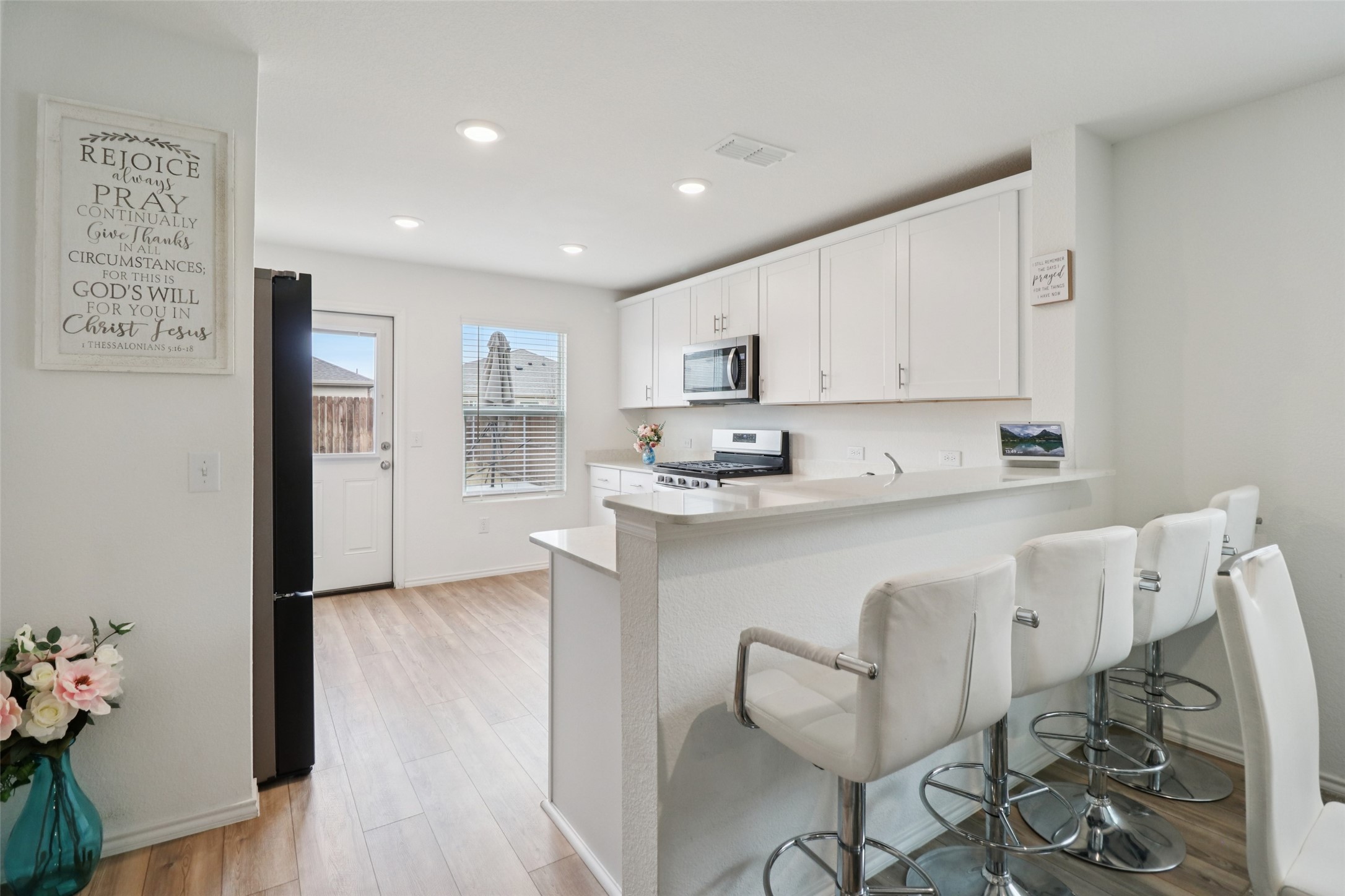 Bright white kitchen with a long breakfast bar, white swivel stools, and light wood-look flooring.