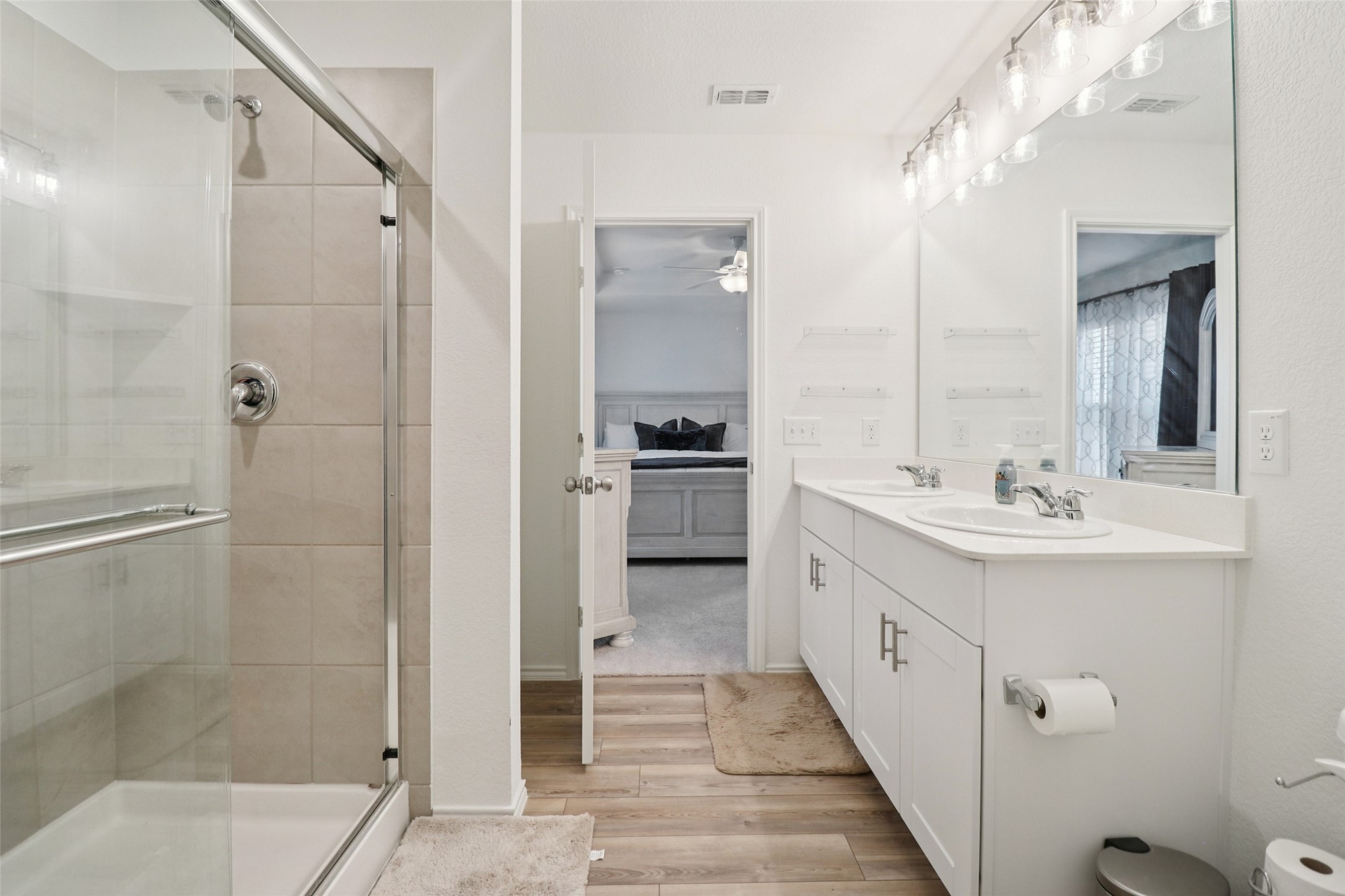 Bathroom with glass shower, double-sink vanity, and doorway opening to a bedroom.