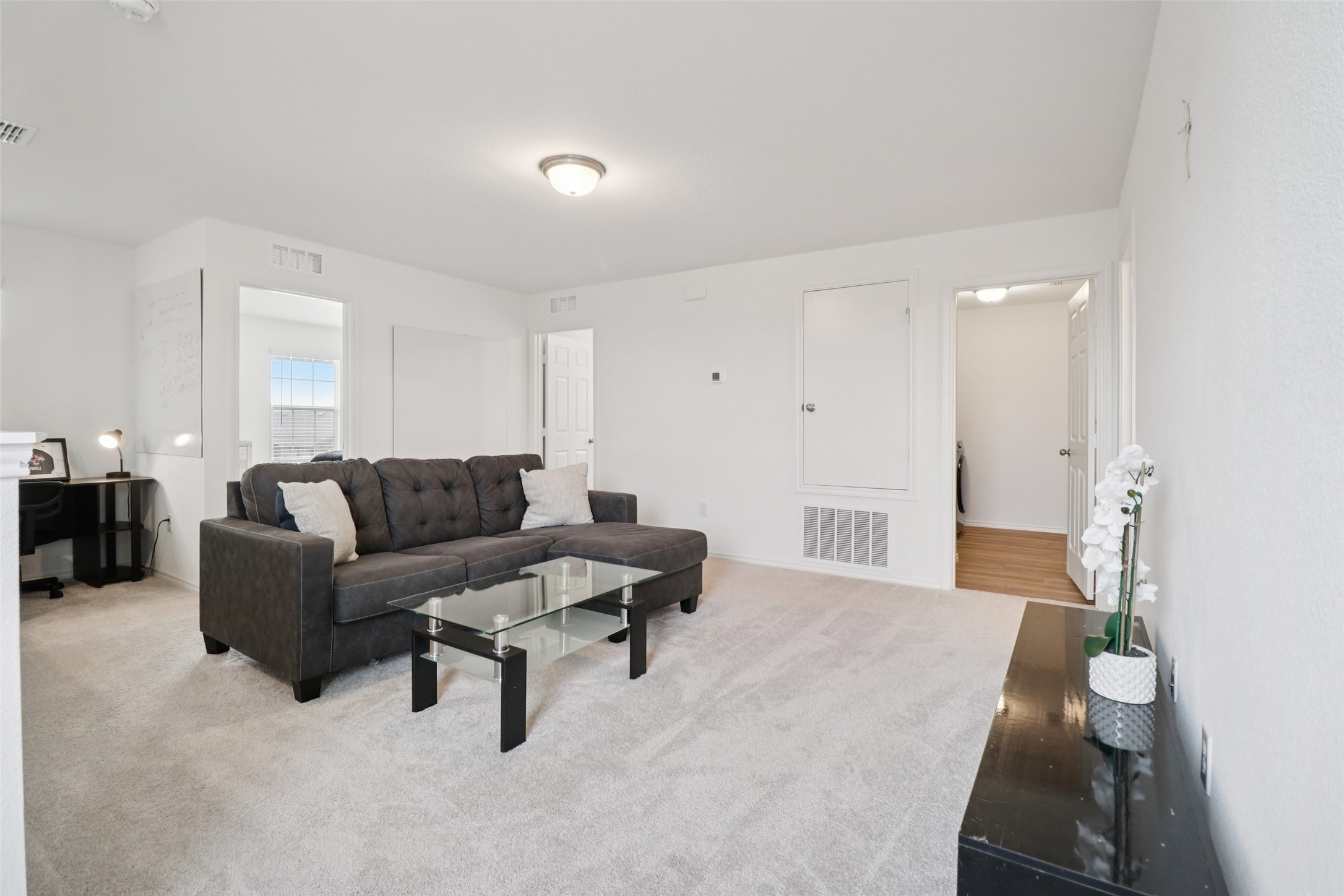 Living room with a dark gray sectional, glass coffee table, and light carpet.