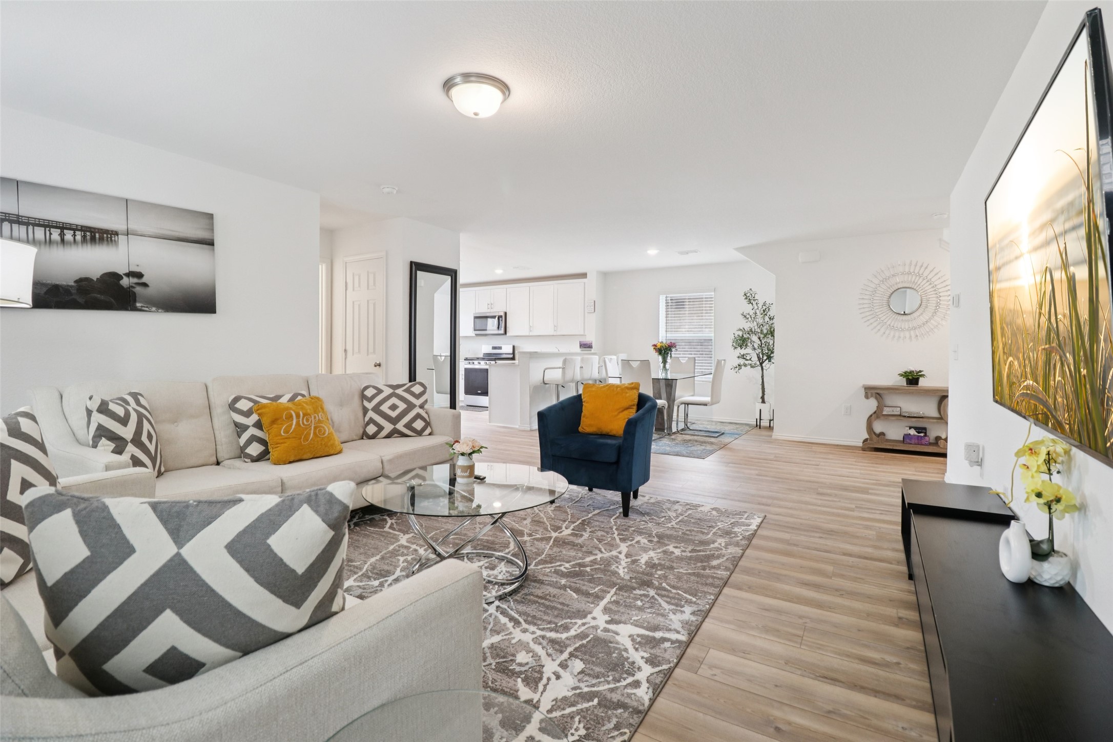 Open-plan living room with a light sectional, blue chair, and the white kitchen and dining area beyond.
