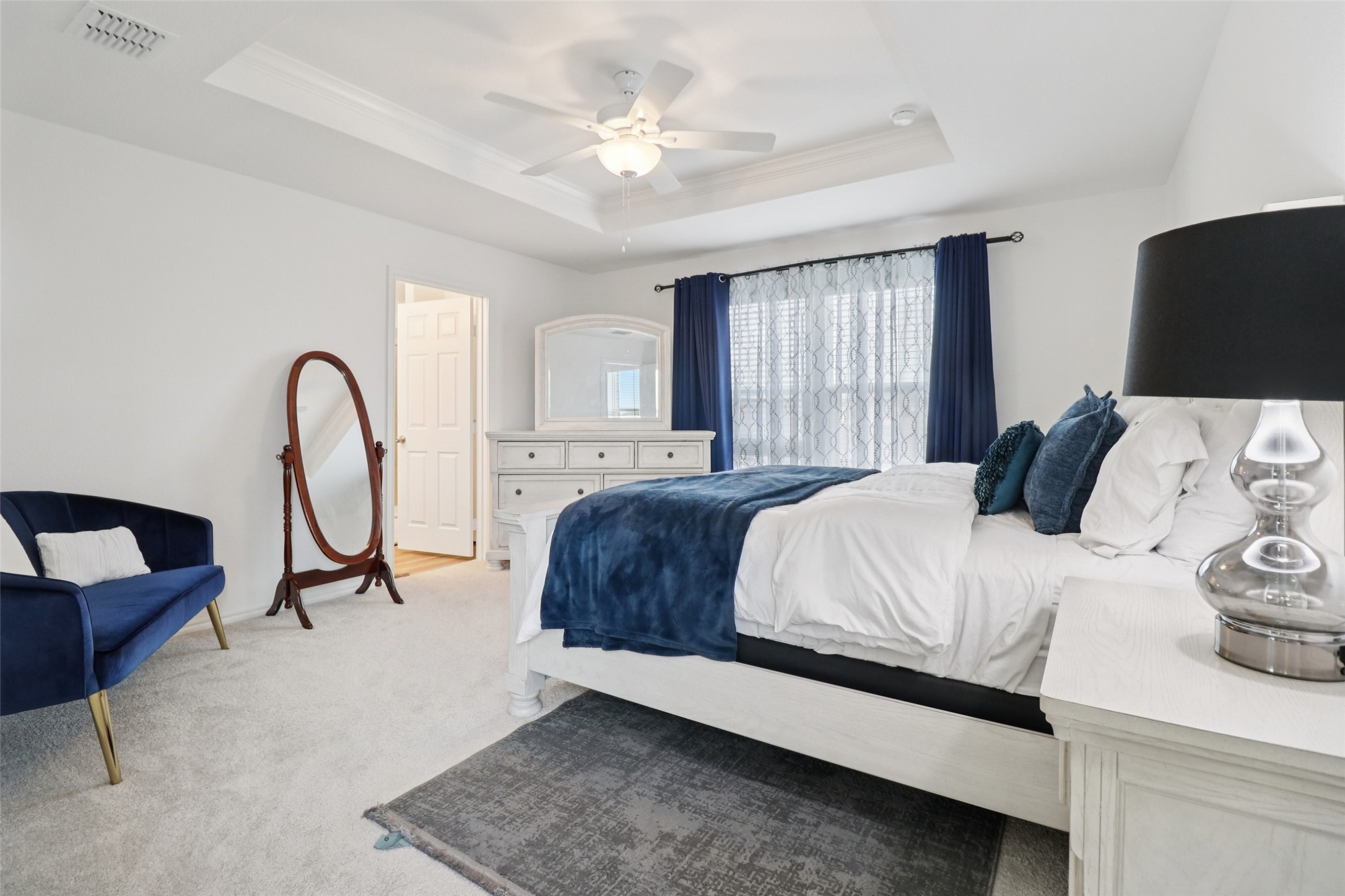 Bedroom with a white bed, navy accents, blue armchair, and full-length standing mirror.